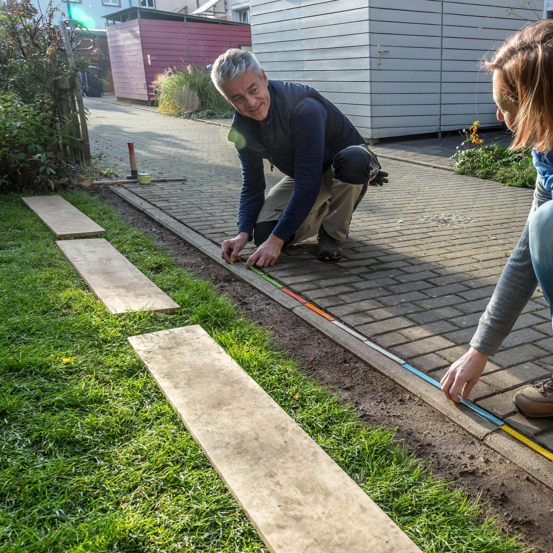 Zwei Personen nehmen Maß für die Punktfundamente, um einen Zaun aufzustellen.