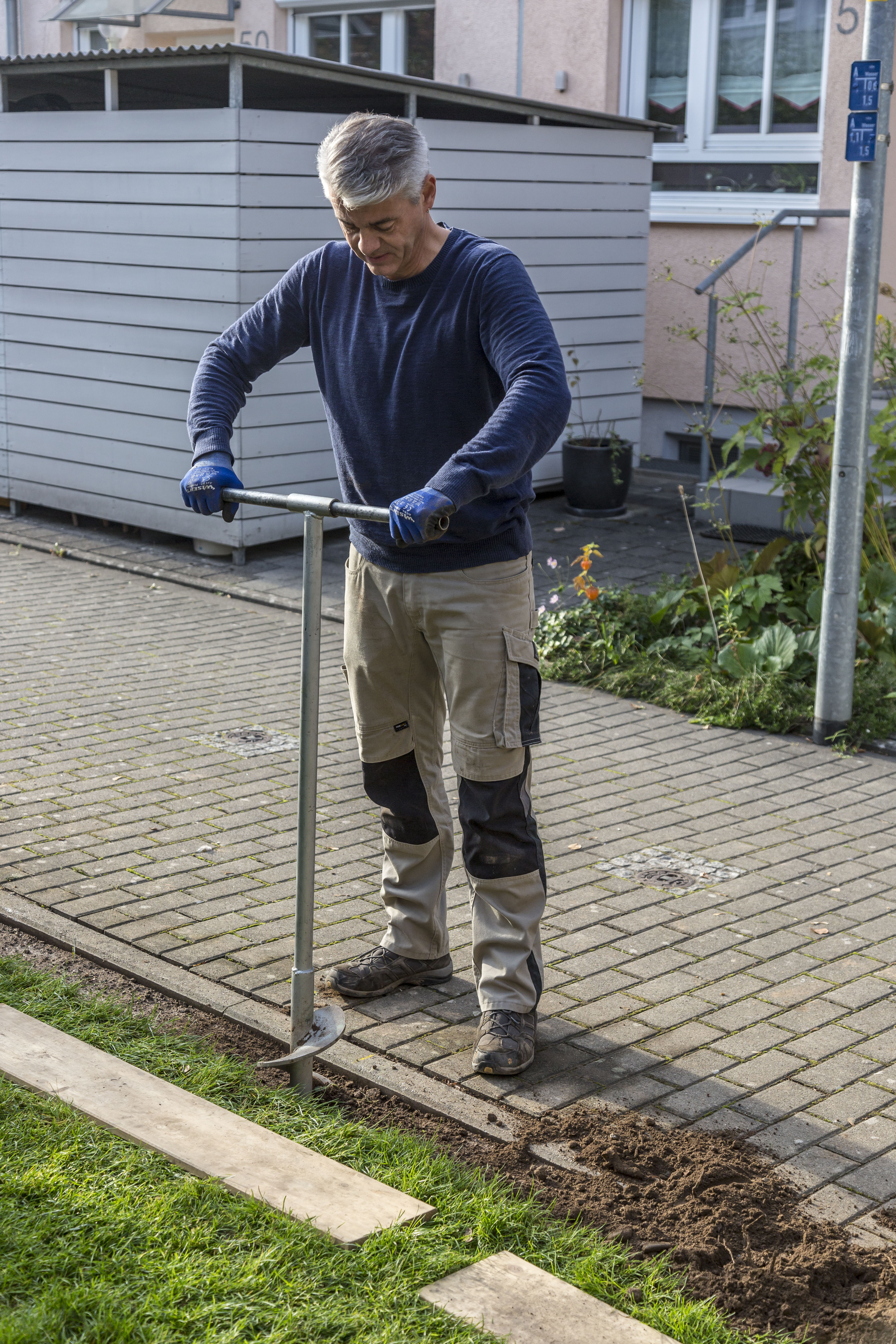 Ein Mann bohrt mit einem Erdbohrer ein Loch für ein Fundament.