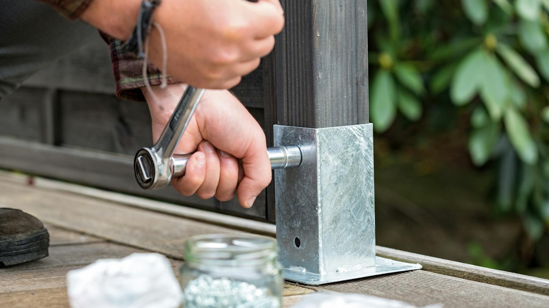 Zaunpfosten wird in einer Metallhalterung am Bodenbelag festgeschraubt.