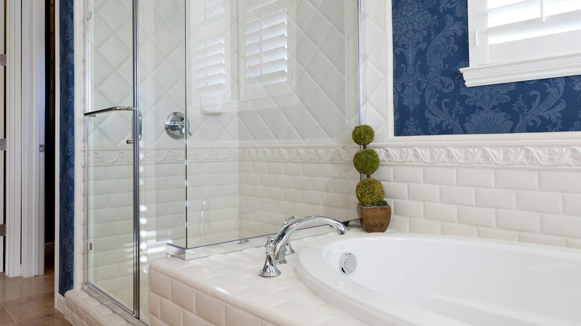 Badezimmer mit Dusche und Badewanne vor einer blauen Mustertapete