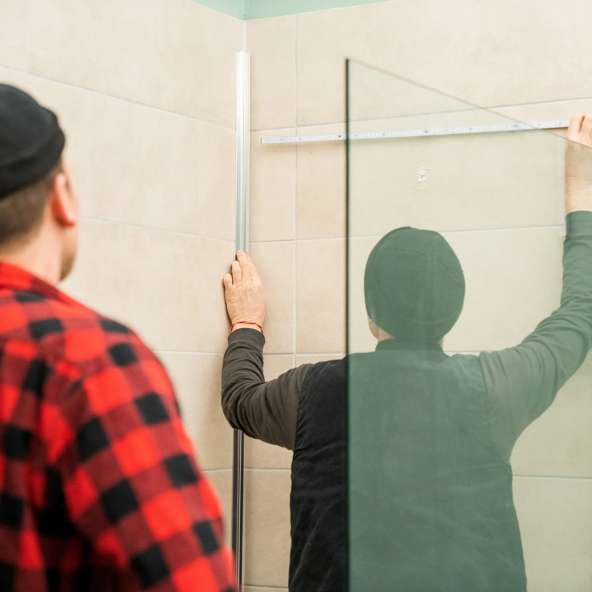 Zwei Handwerker messen die Breite einer Dusche mit Fliesenspiegel aus.