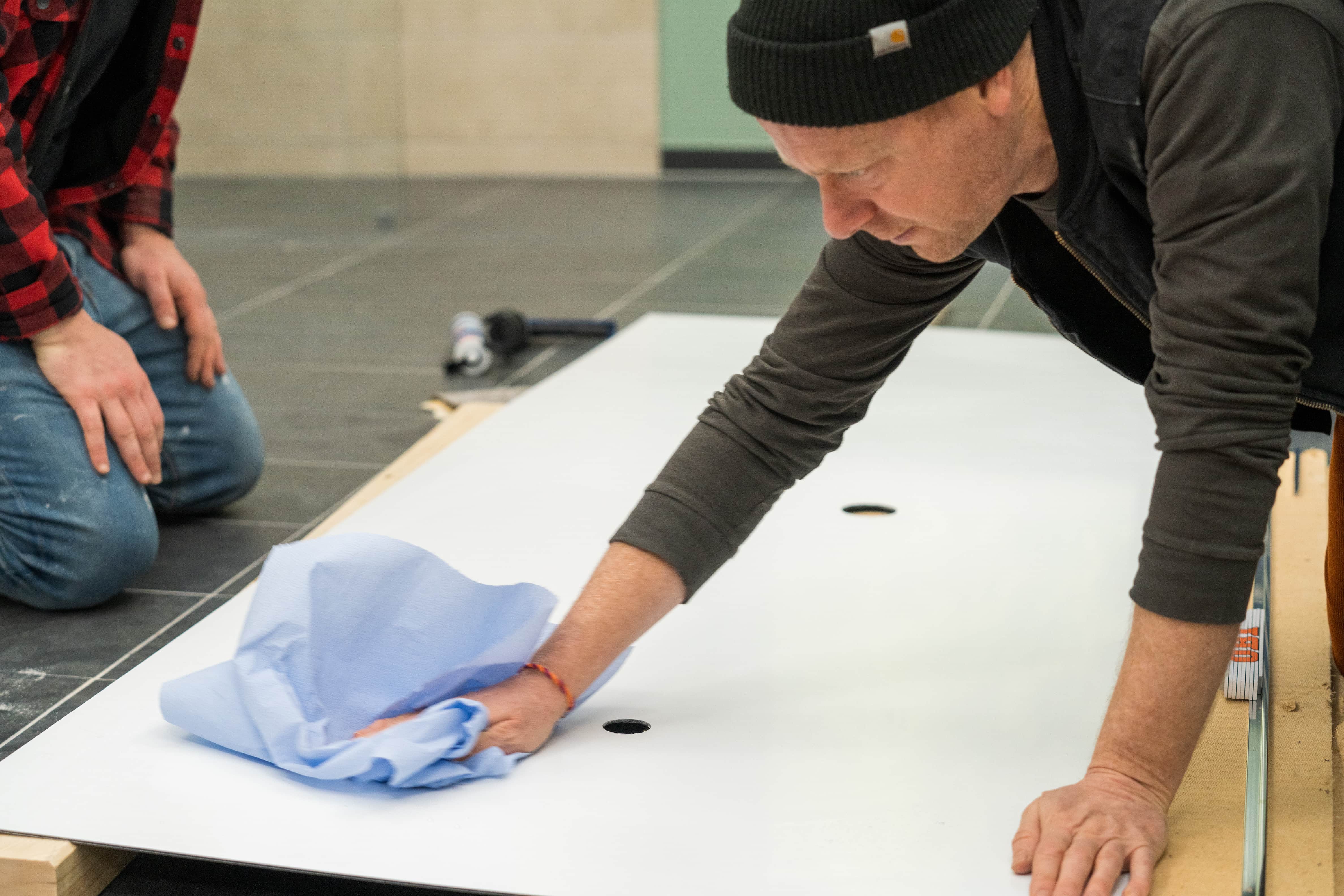 Eine Person reinigt die Rückseite einer Duschrückwand mit blauen Tüchern.