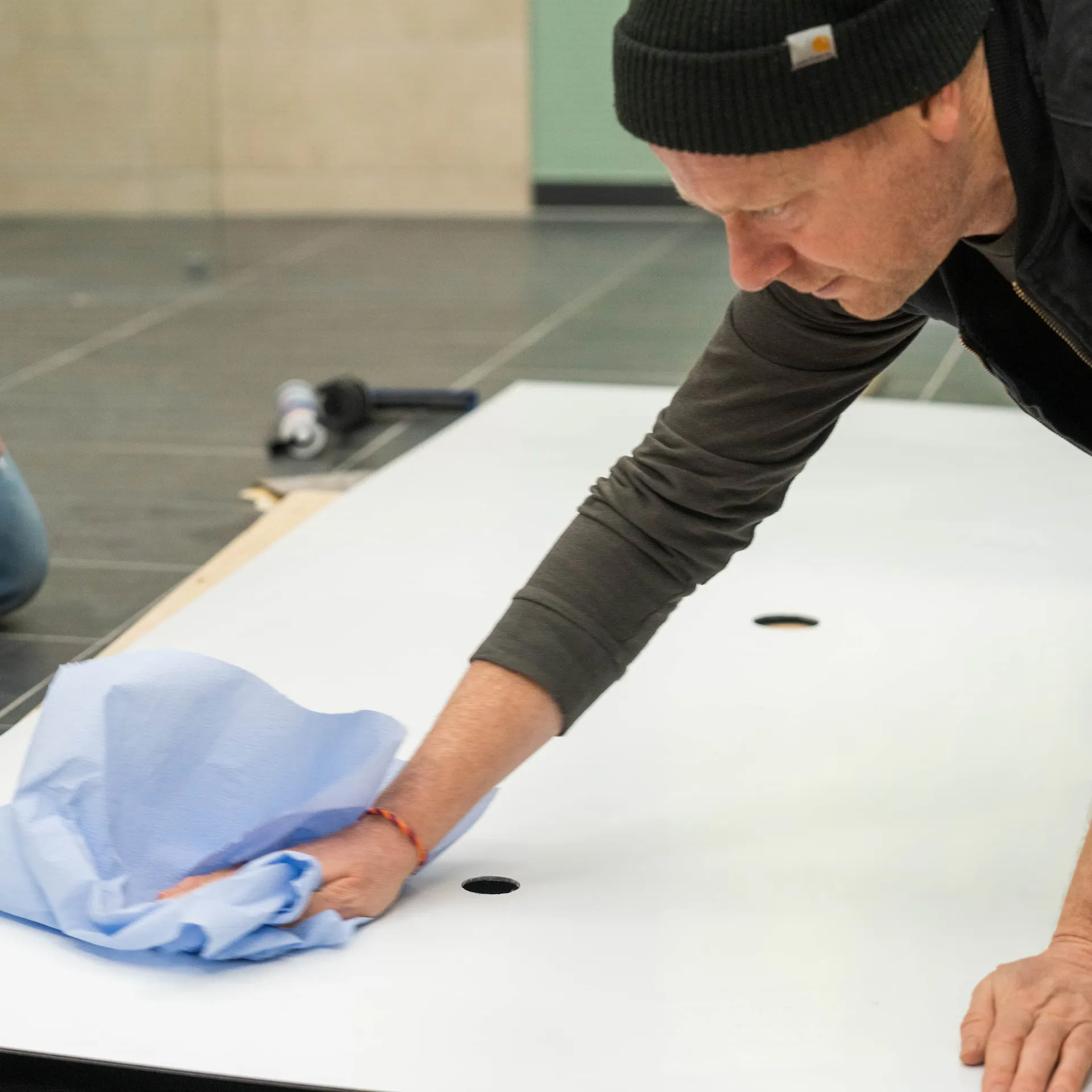 Eine Person reinigt die Rückseite einer Duschrückwand mit blauen Tüchern.