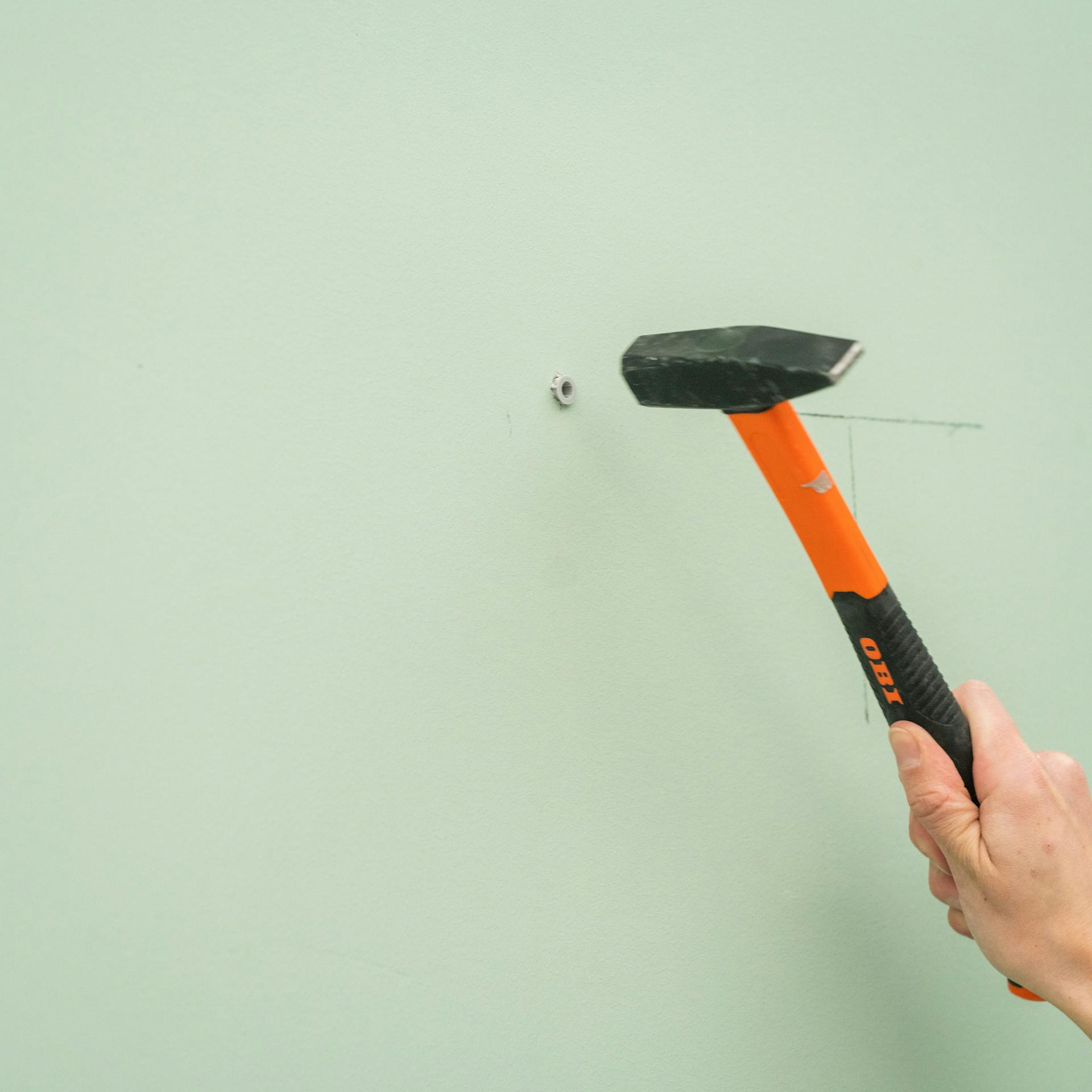 Jemand schlägt einen Dübel in eine Wand.