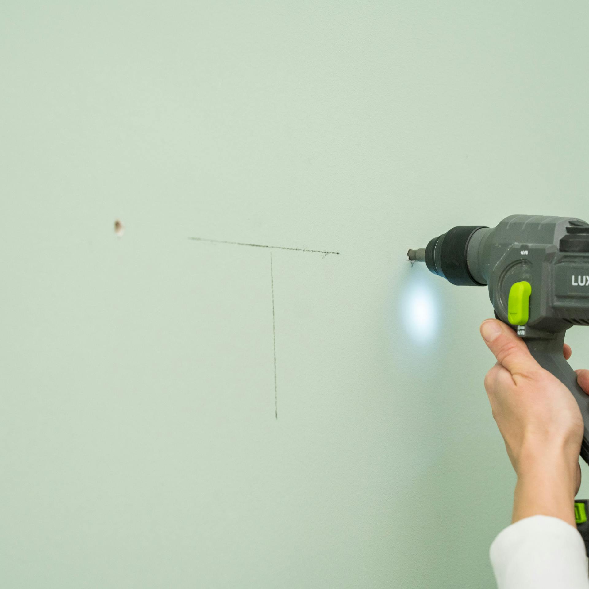 Jemand bohrt die Löcher für die Wandbefestigung eines Spiegelschrankes.