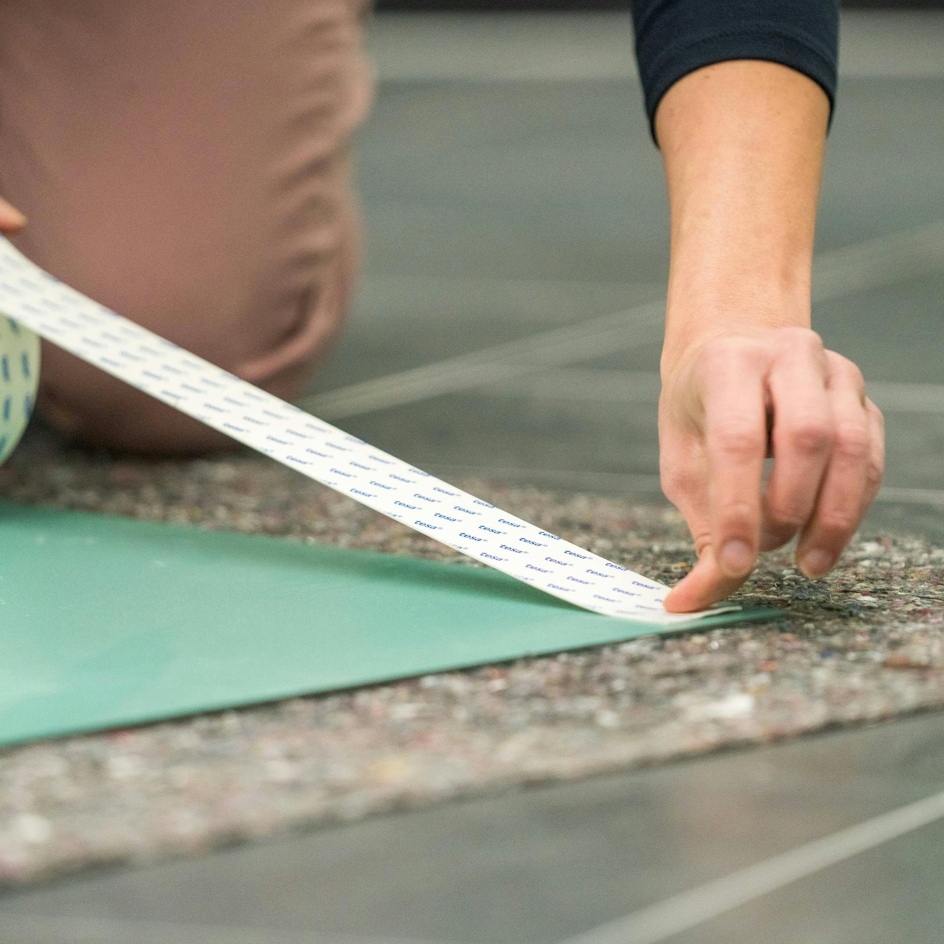 Jemand bringt doppelseitiges Klebeband auf der Rückseite eines Spiegels an.