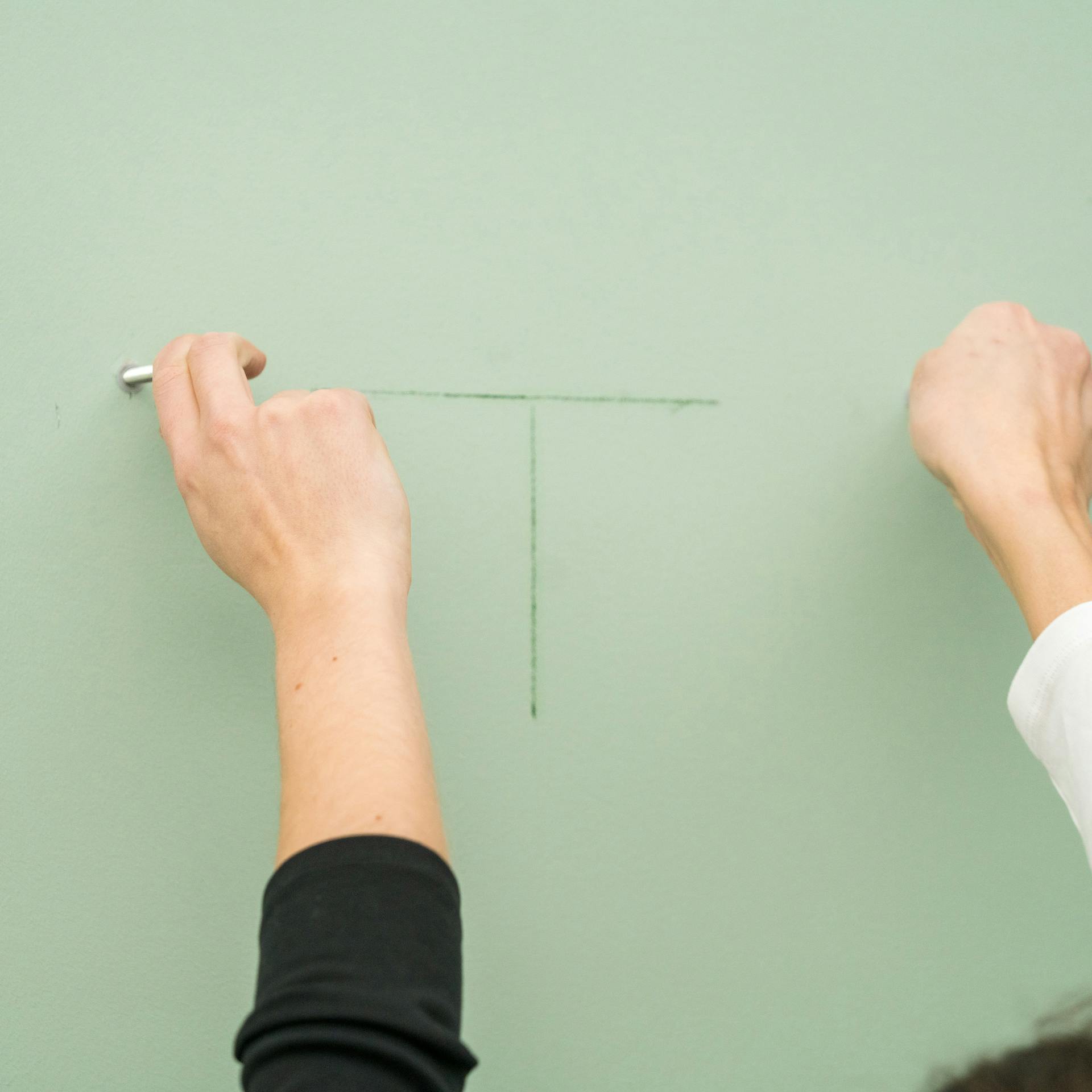 Handwerker markieren Positionen für Bohrlöcher an einer hellgrünen Badezimmerwand mit Bleistift.