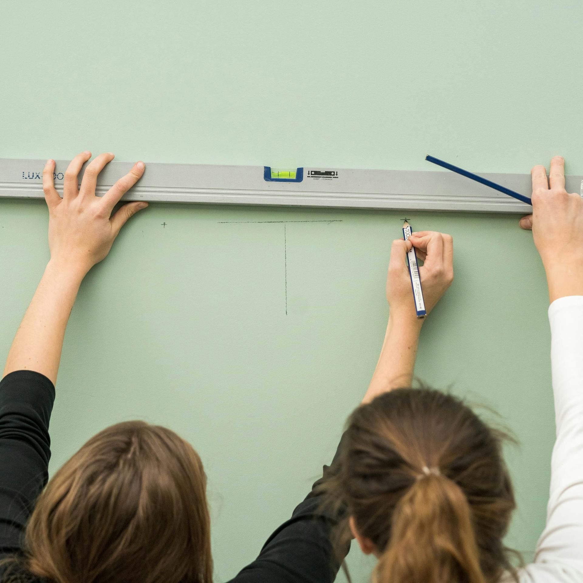 Zwei Handwerkerinnen markieren die Position für einen Wandspiegel mit einer Wasserwaage.