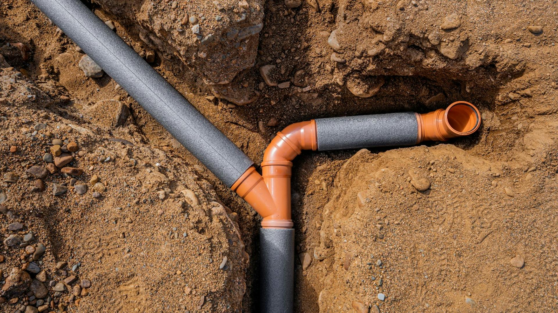 Verzweigte Abwasserrohre in einem ausgehobenen Erdgraben