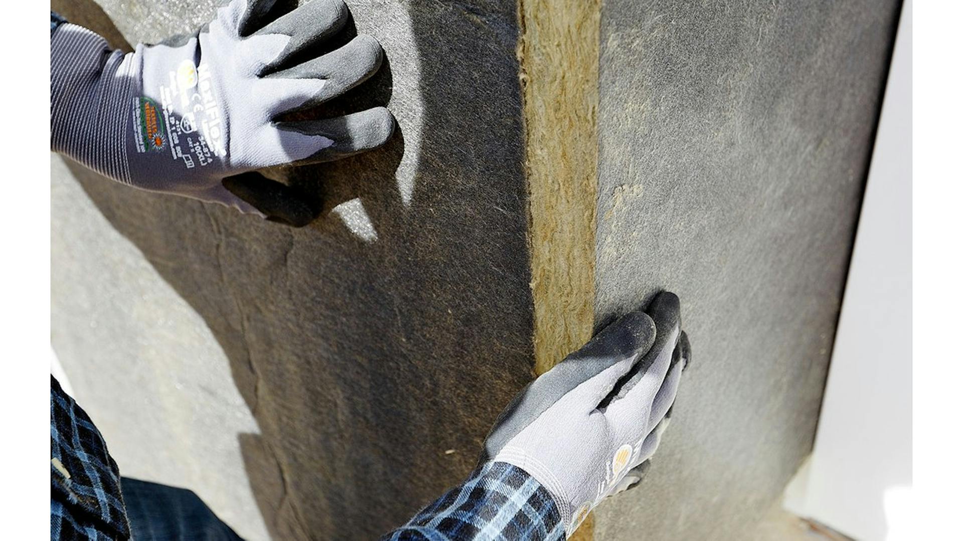 Heimwerker in Arbeitshandschuhen dämmt Außenfassade mit Steinwolle.