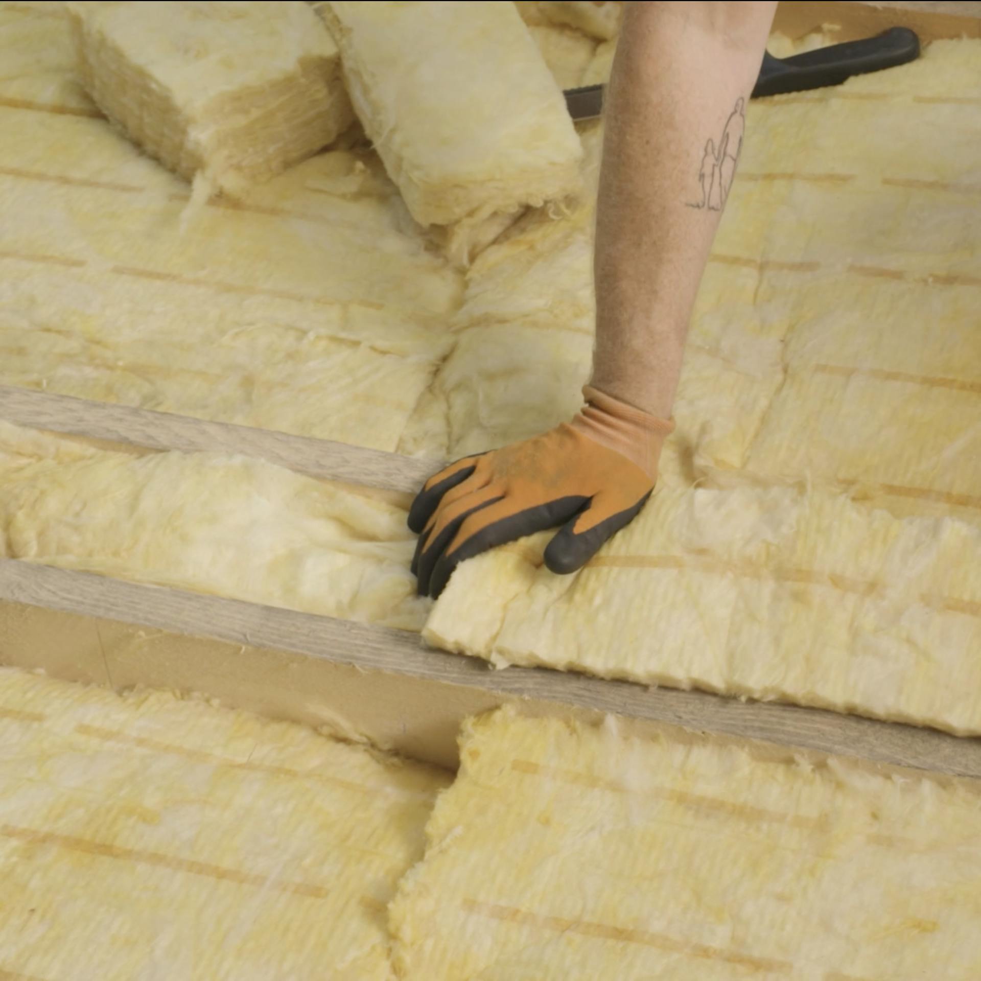 Dämmwolle wird von Handwerker zwischen den Balken auf dem Boden ausgelegt.