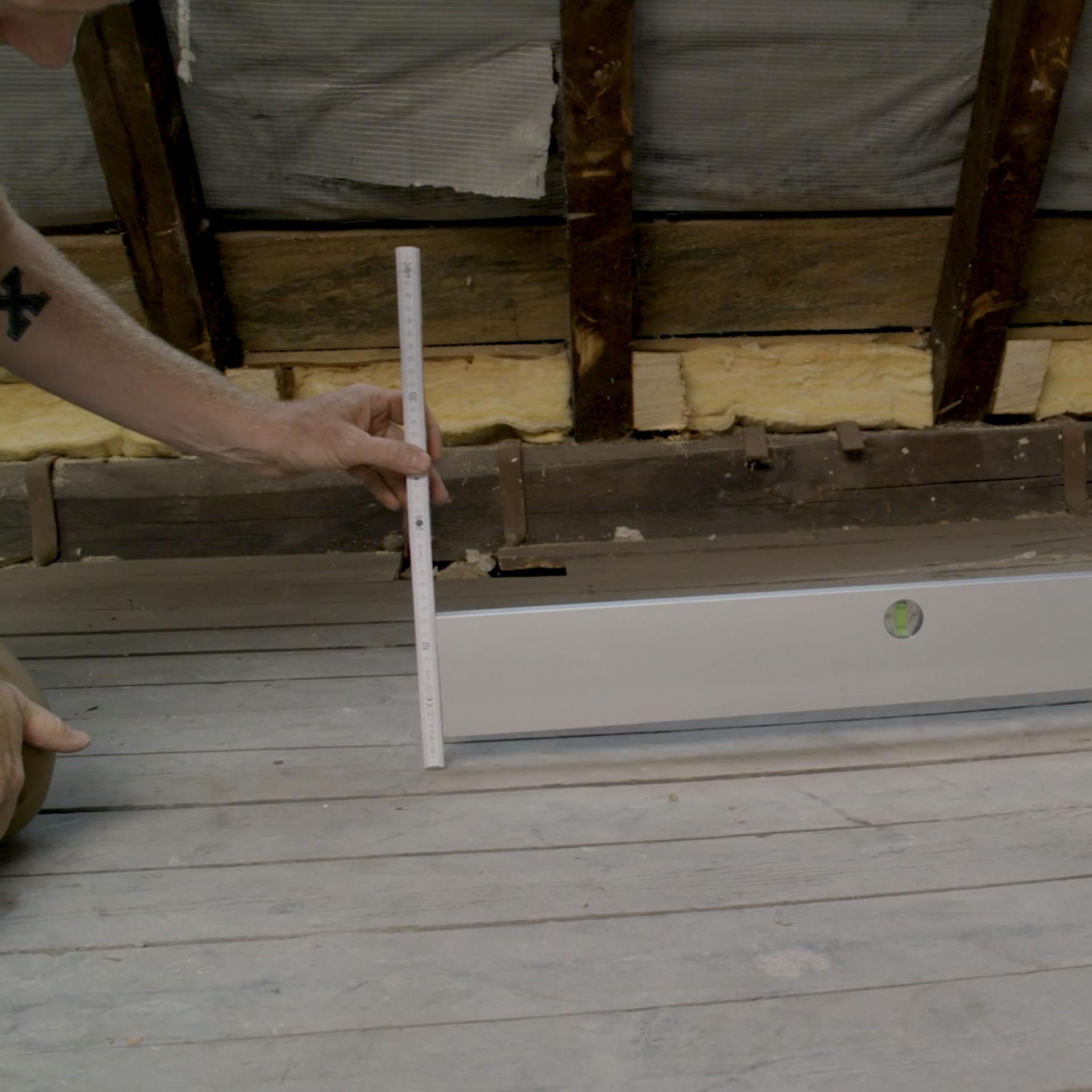 Lange Wasserwaage auf Boden platziert und Zollstock wird darangehalten.