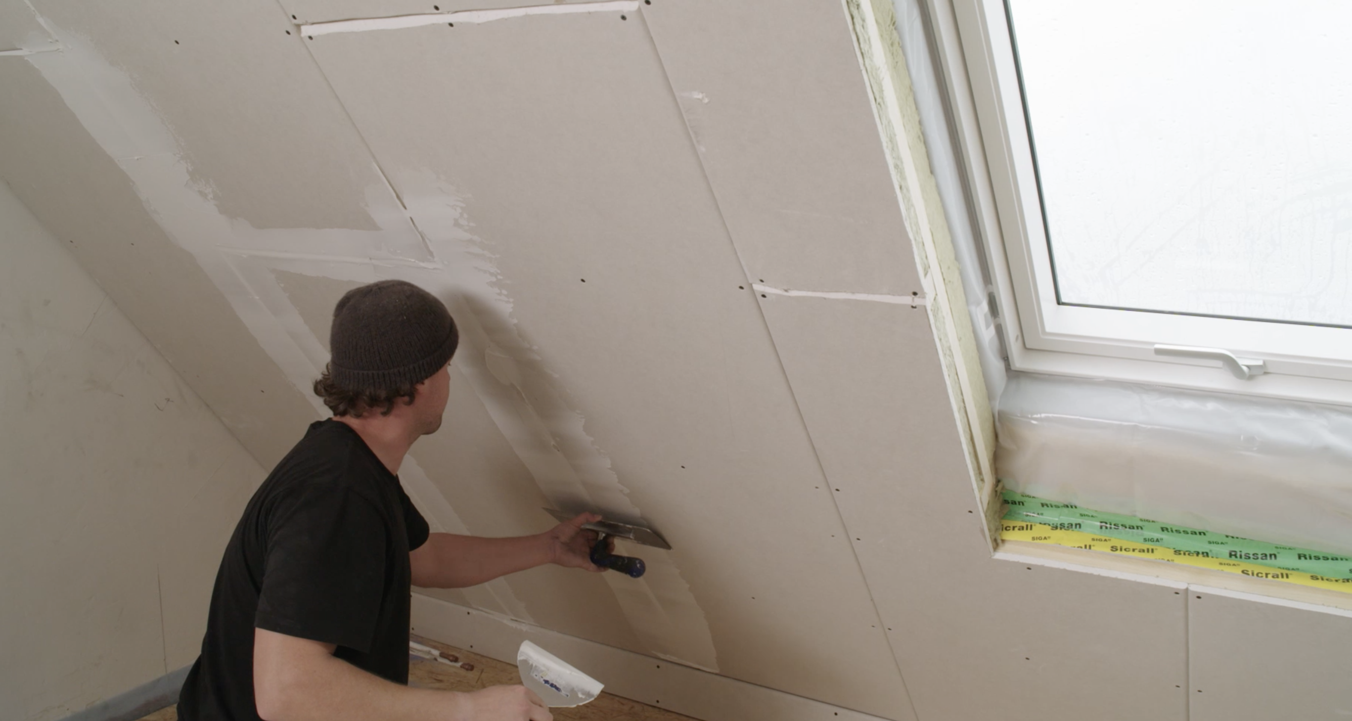Ein Handwerker trägt Spachtelmasse auf die Dachschräge auf. 