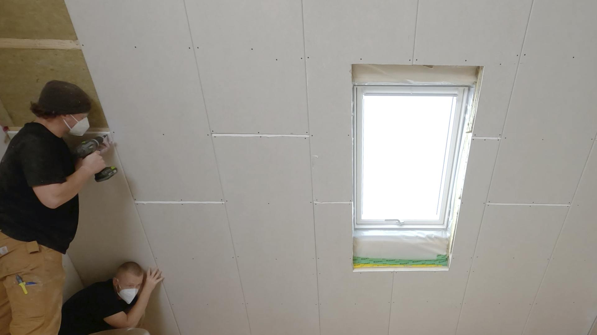 Zwei Handwerker stehen an einer Dachschräge und schrauben Gipskartonplatten an.