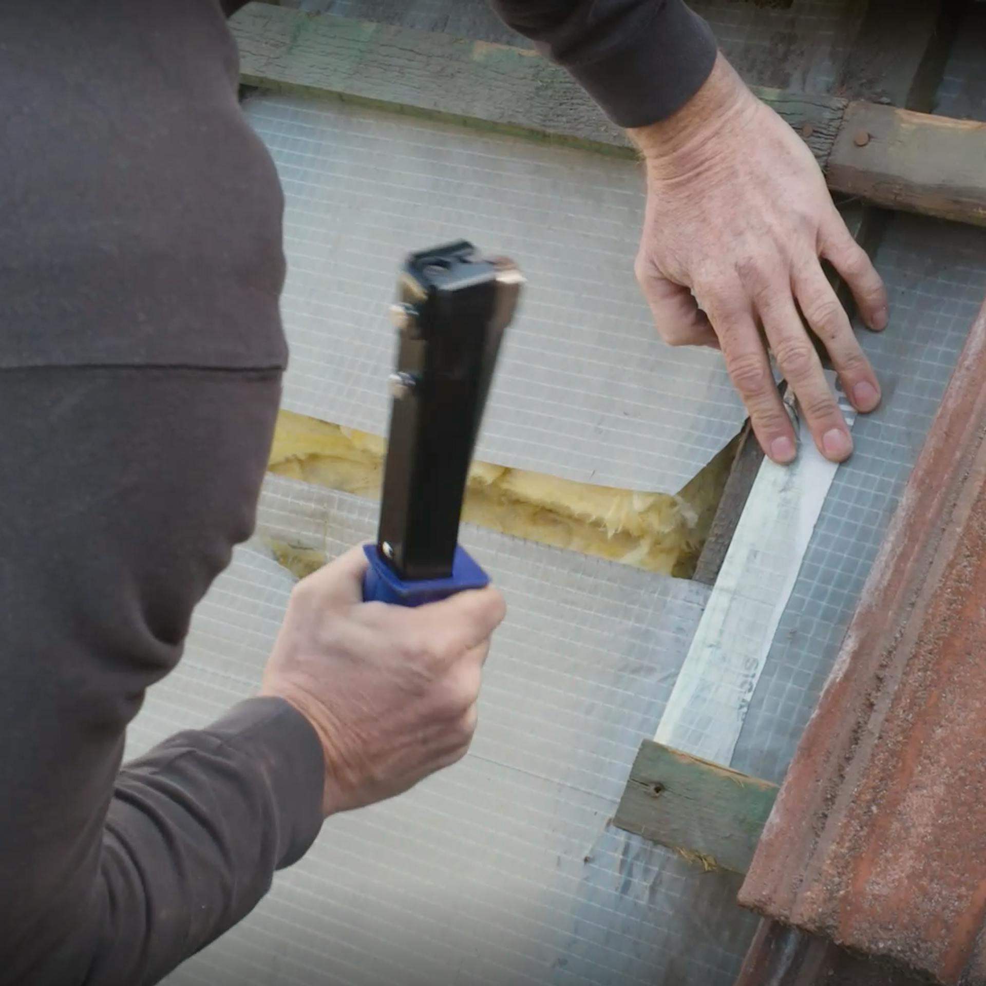 Pracovník upevňuje fóliu podstrešného pásu sponkovačkou.