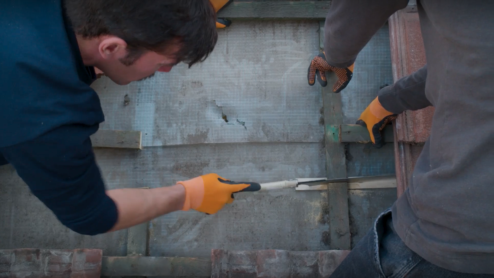 Dvaja pracovníci pília japonskou pílou kontralatu.