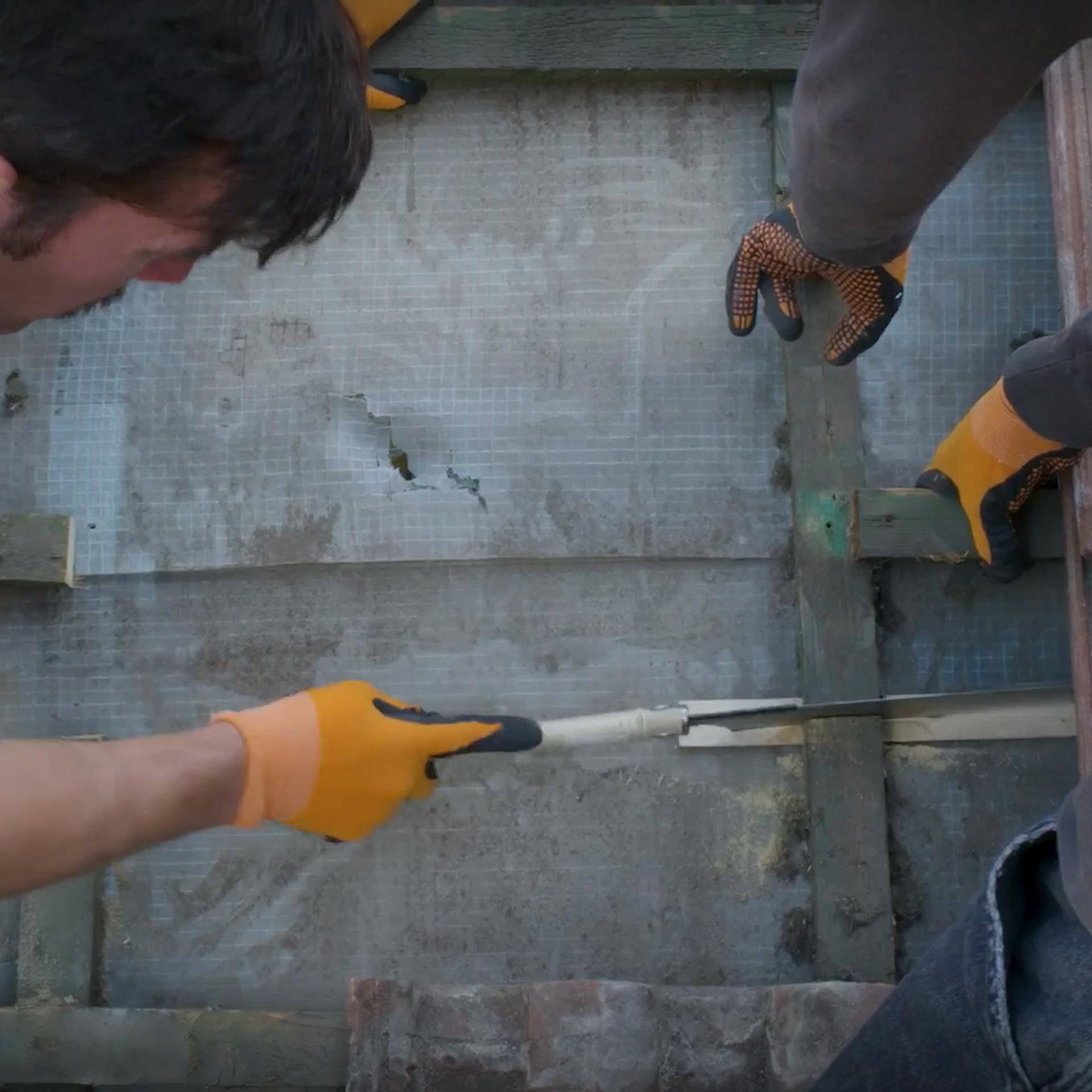 Dvaja pracovníci pília japonskou pílou kontralatu.