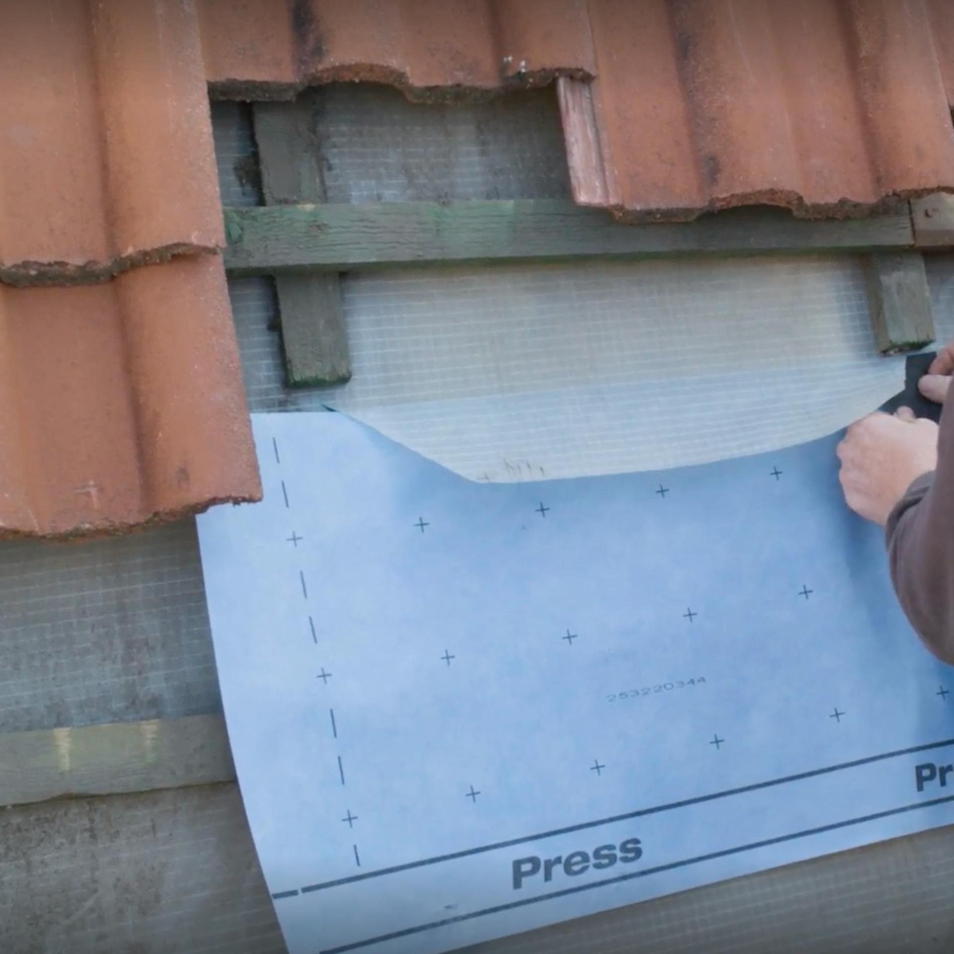 Pracovník ukladá novú fóliu na šikmú strechu.