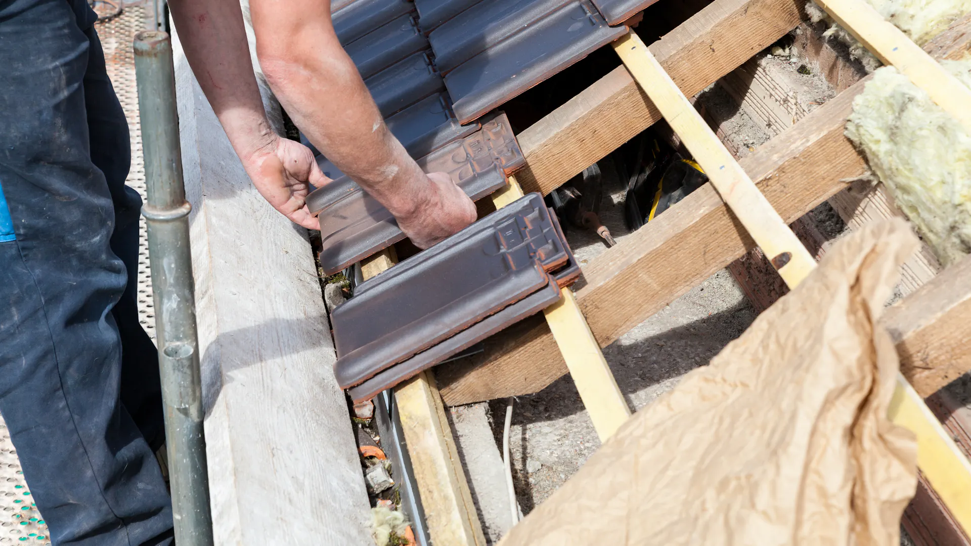 Ein Handwerker tauscht Ziegel an einem Schrägdach aus.