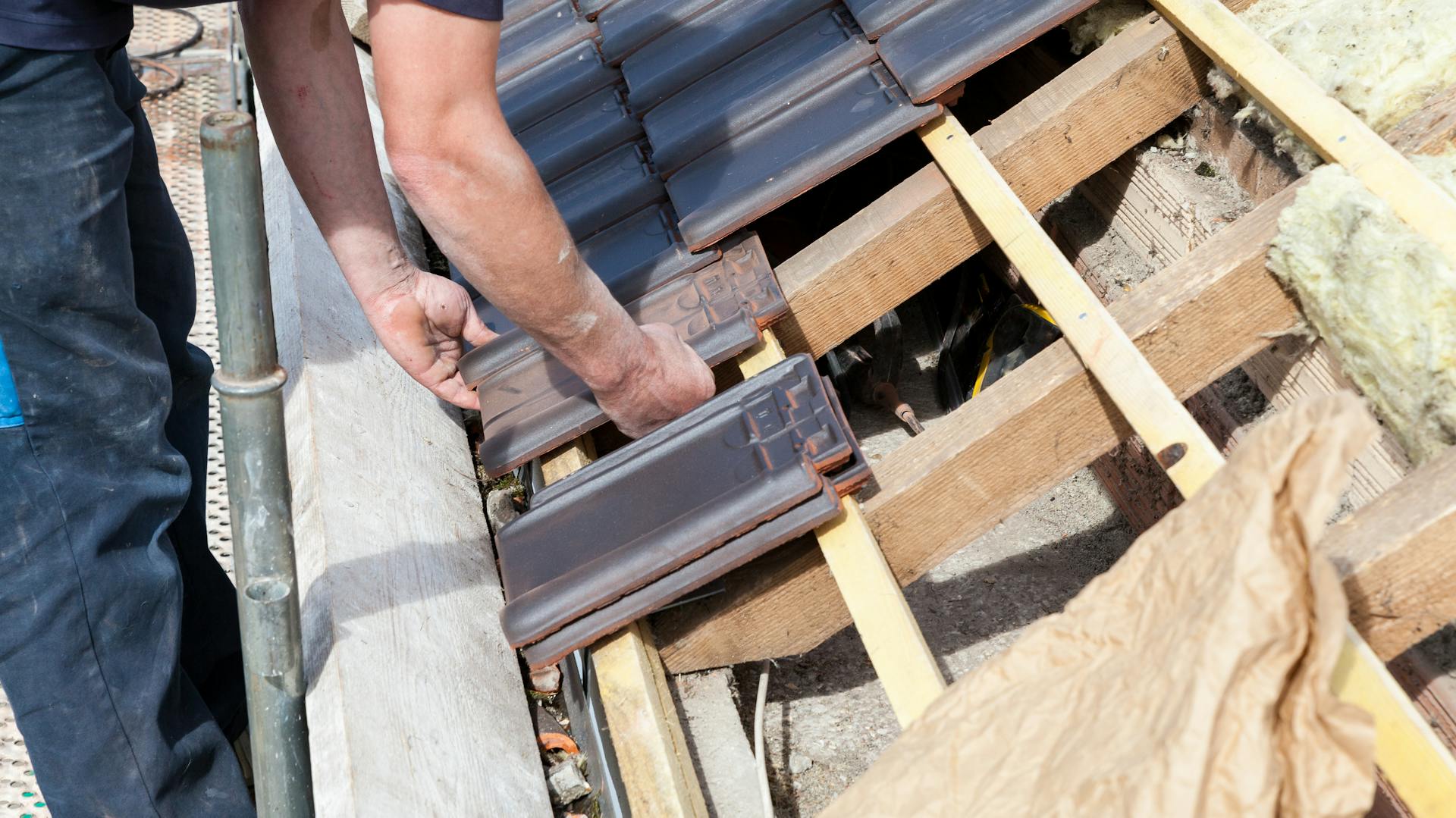 Ein Handwerker tauscht Ziegel an einem Schrägdach aus.