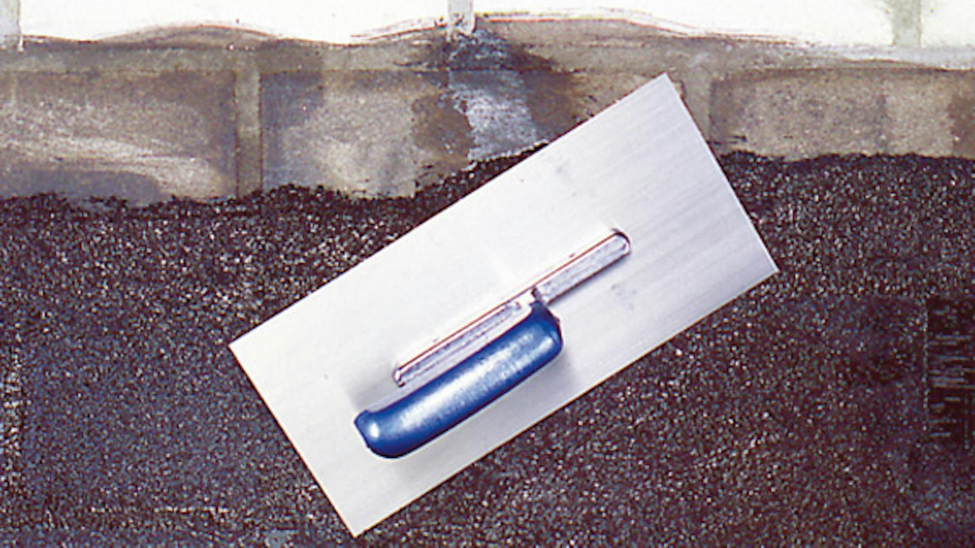 Glättkelle, mit der eine Dichtungsmasse auf Kellerwand verteilt wird.