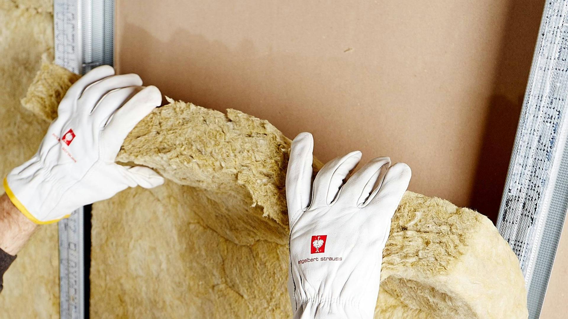 Heimwerker in Arbeitshandschuhen dämmt Fassade mit Dämmstoff.