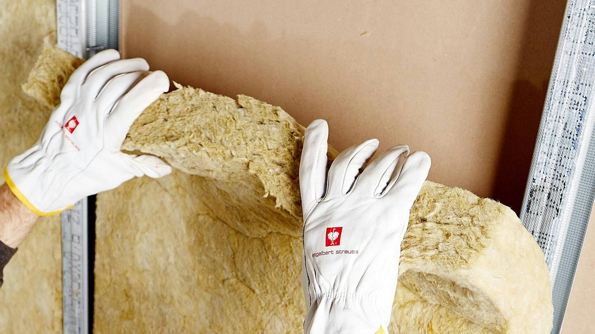 Jemand bringt einen Dämmstoff an eine Wand an.