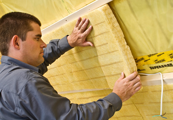 Egy személy a szarufák alá szigetelést helyez el.