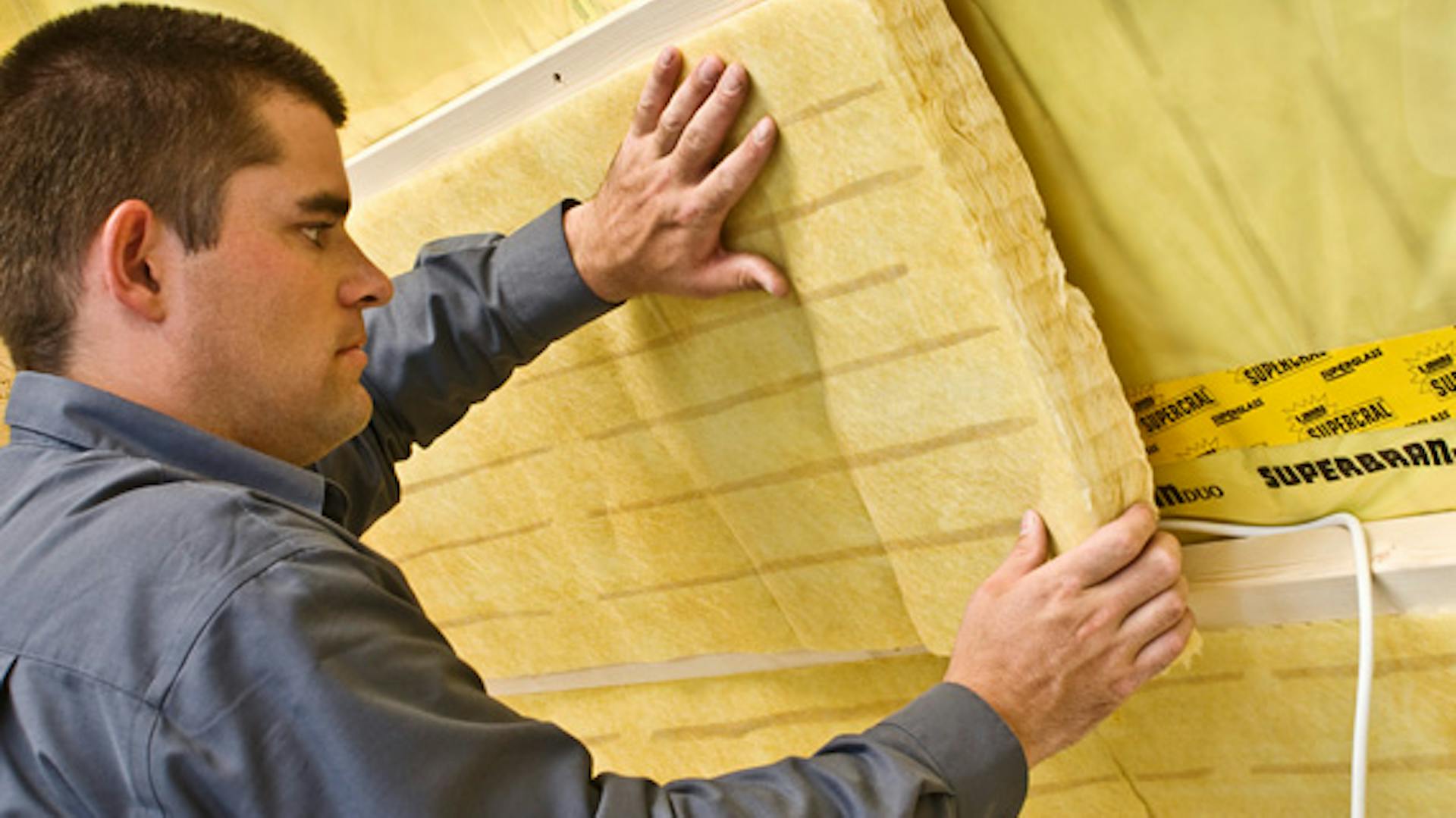 Egy személy a szarufák alá szigetelést helyez el.