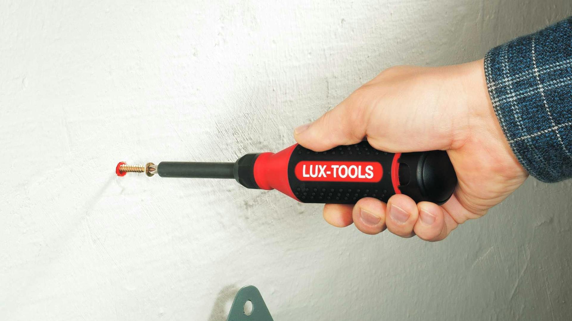 Hand schraubt Schraube mit Schraubenzieher in Wand