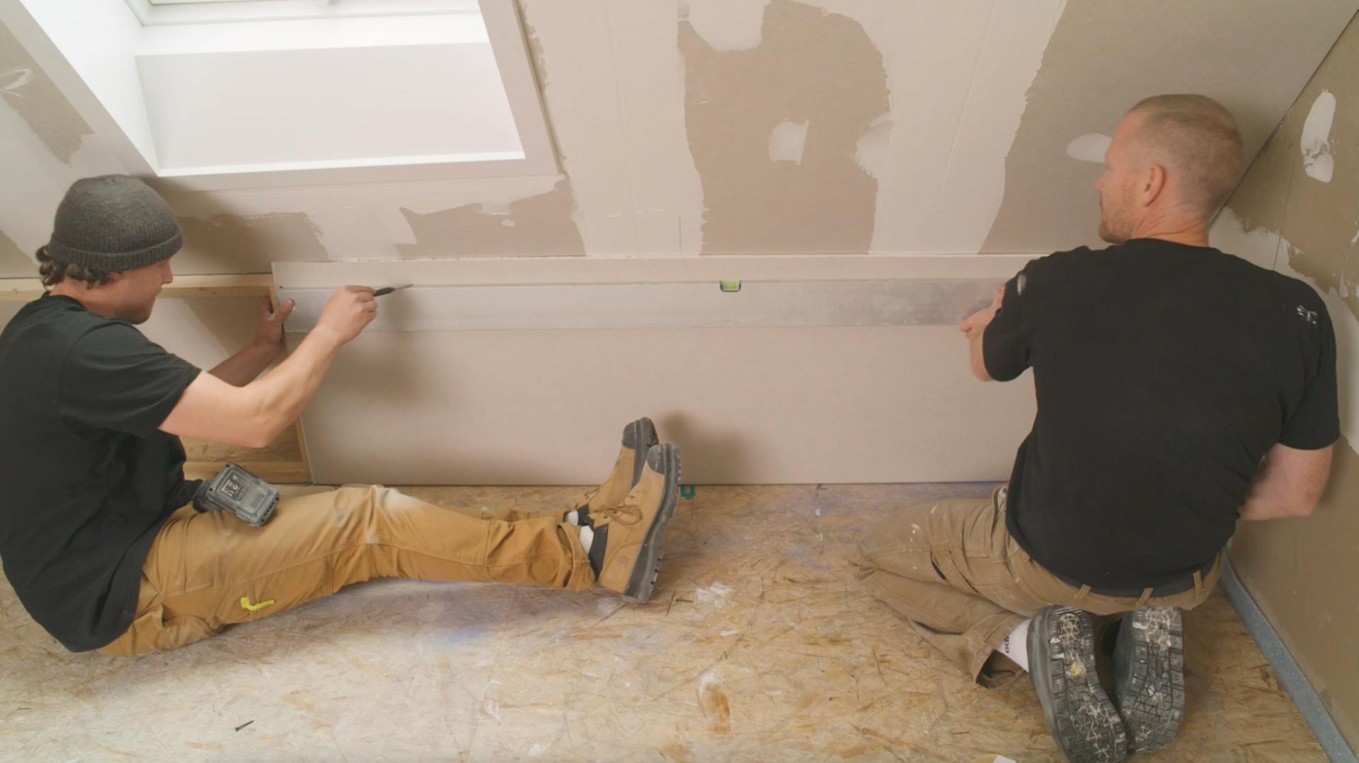Zwei Handwerker stehen vor einer Dachschräge und halten Dämmwollplatten an der Wand an.