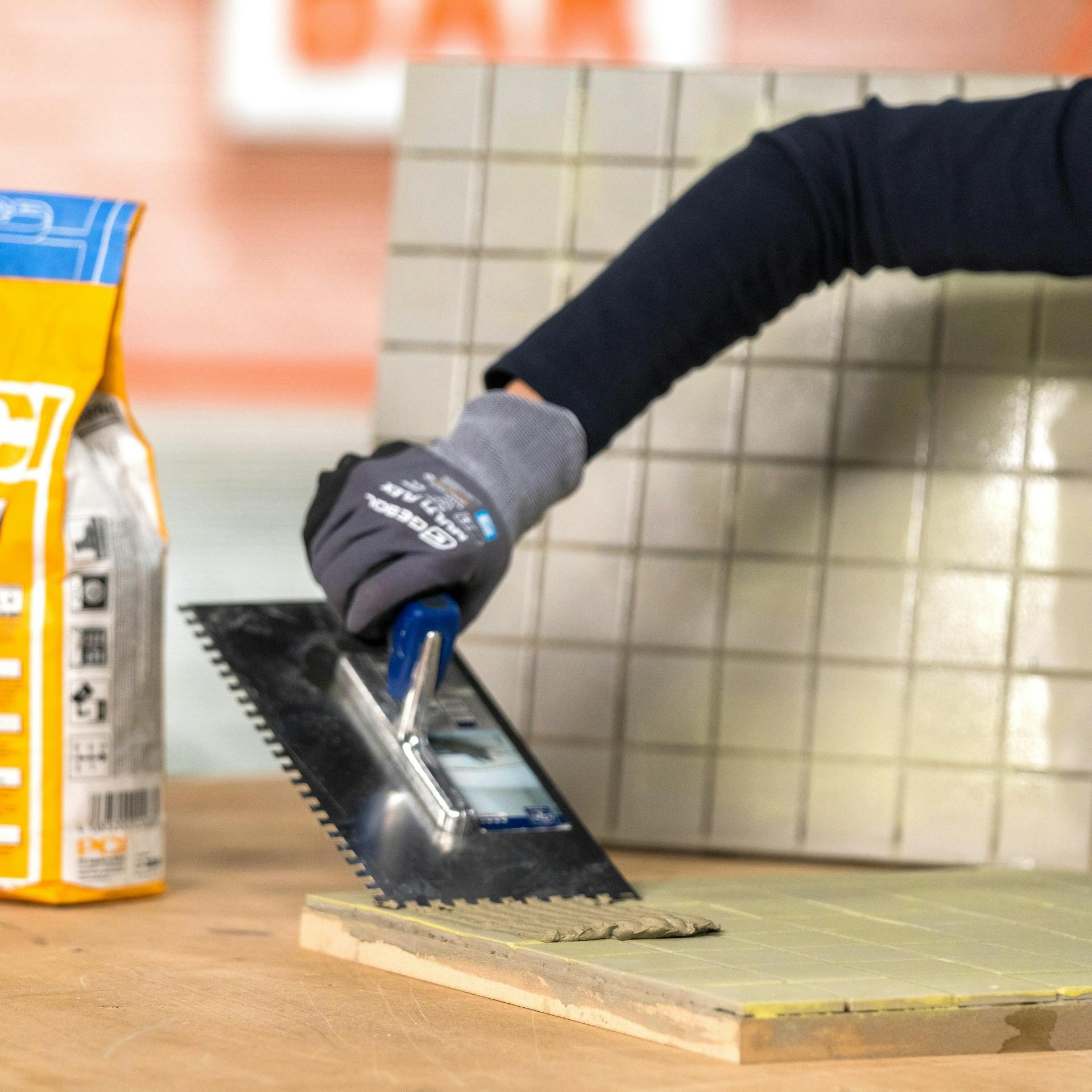 Handwerker trägt Fliesenkleber auf den Untergrund auf.