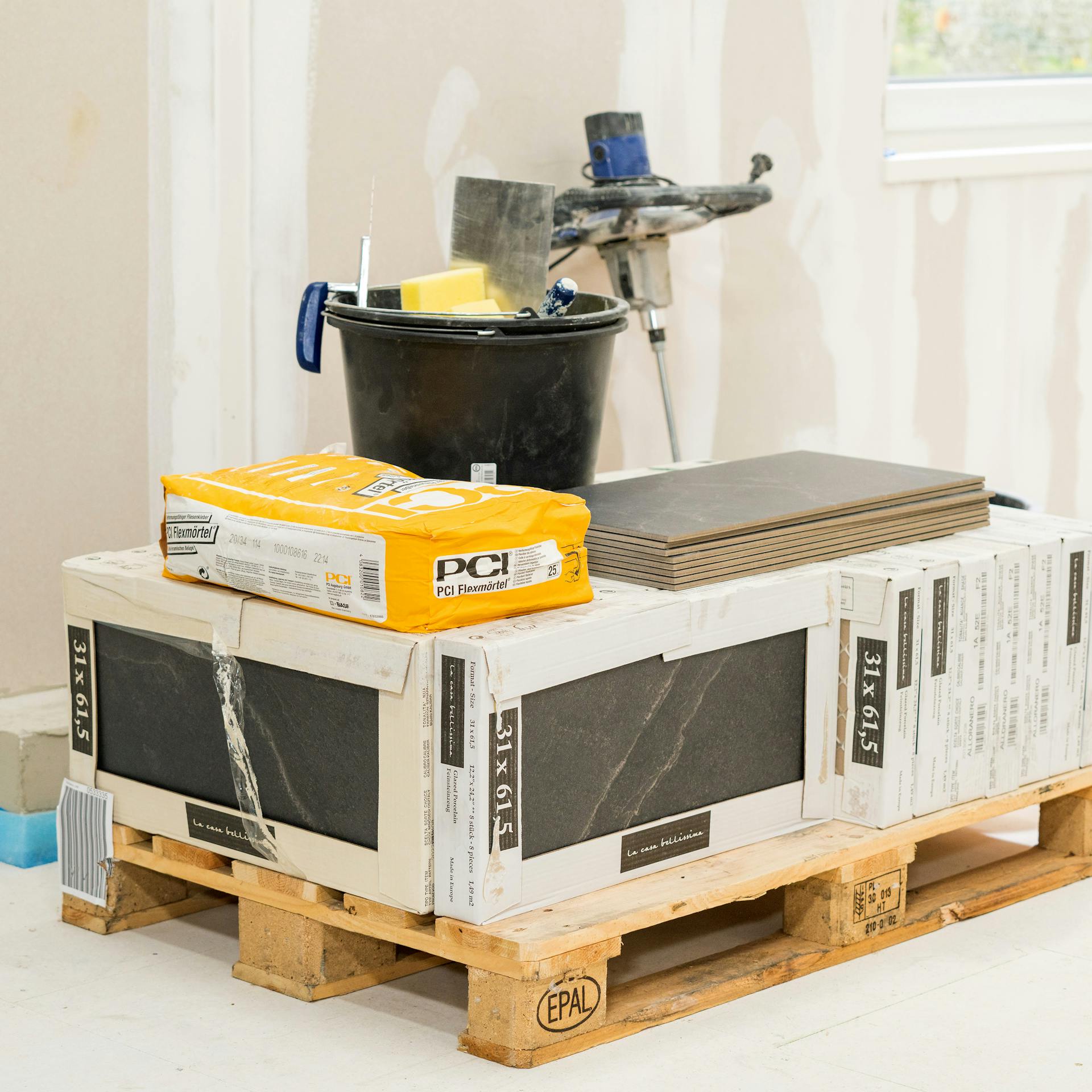 Fliesen und Fliesenkleber liegen auf einer Palette.