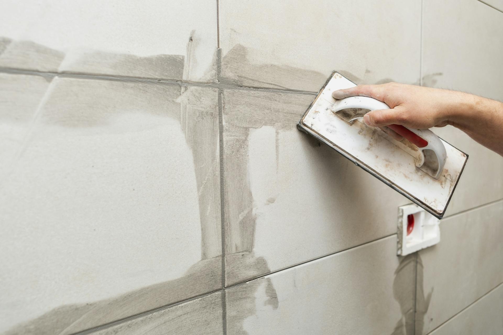 Una persona stucca le fughe delle piastrelle con malta nuova.