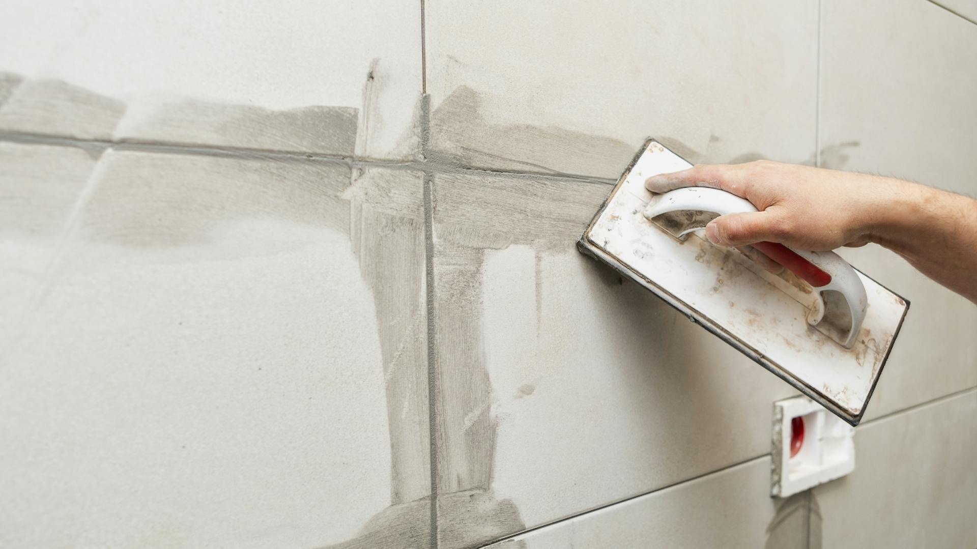 Person verfugt Fliesen neu mit Mörtel.