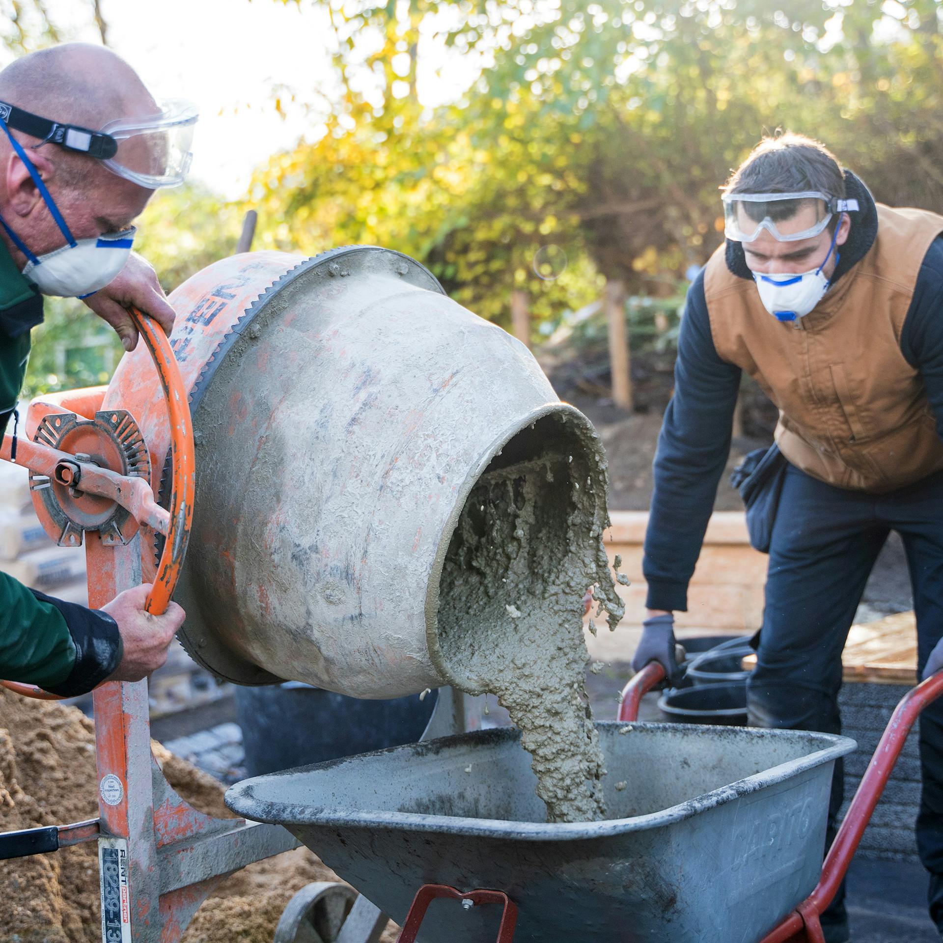 Zwei Männer mischen Beton mit einem Betonmischer.