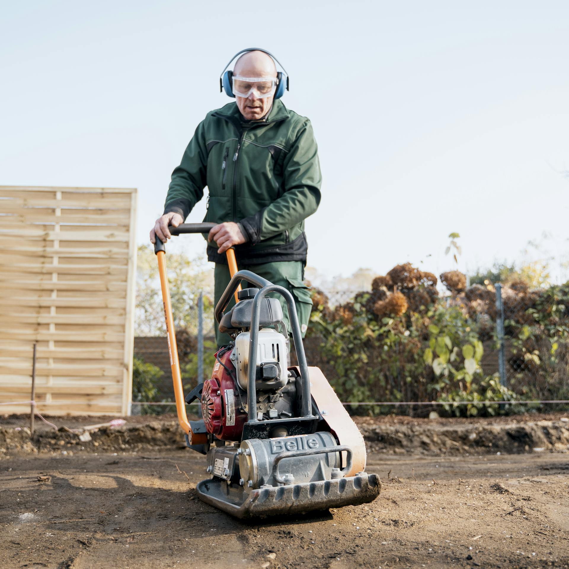 Ein Mann verdichtet den Boden mit einer Rüttelplatte.