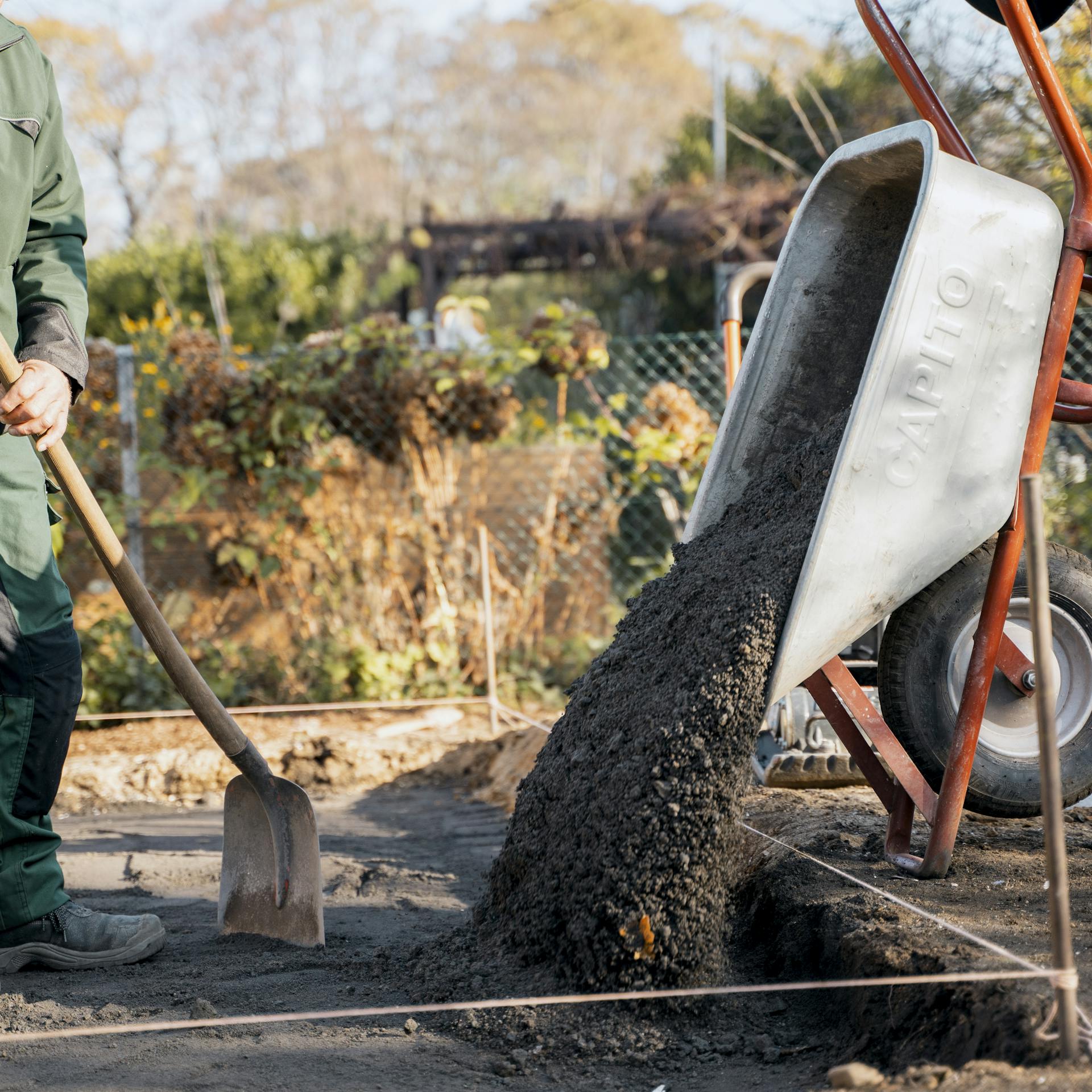 Zwei Personen füllen Schotter in den Bodenaushub.