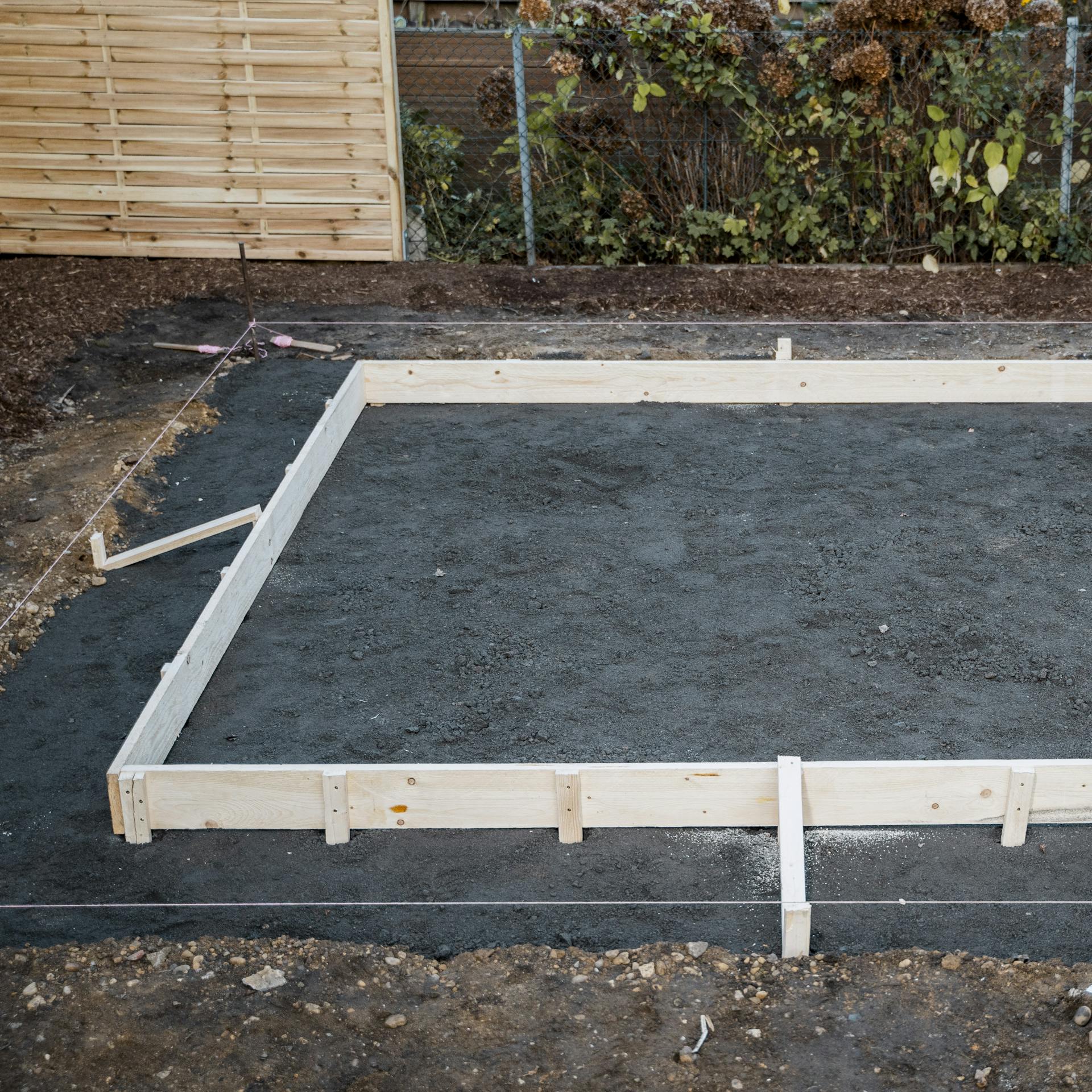 Holzschalungsrahmen auf ausgehobener Schotterfläche im Garten