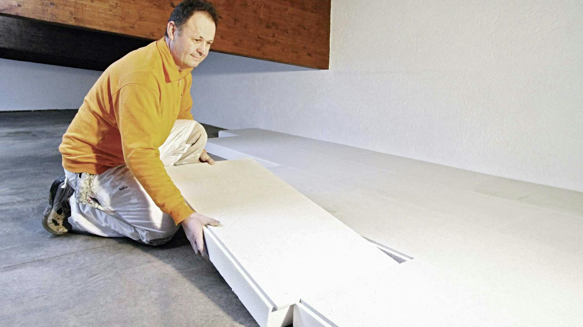 Ein Mann dämmt die oberste Geschossdecke mit einer Kalziumsilikatplatte.