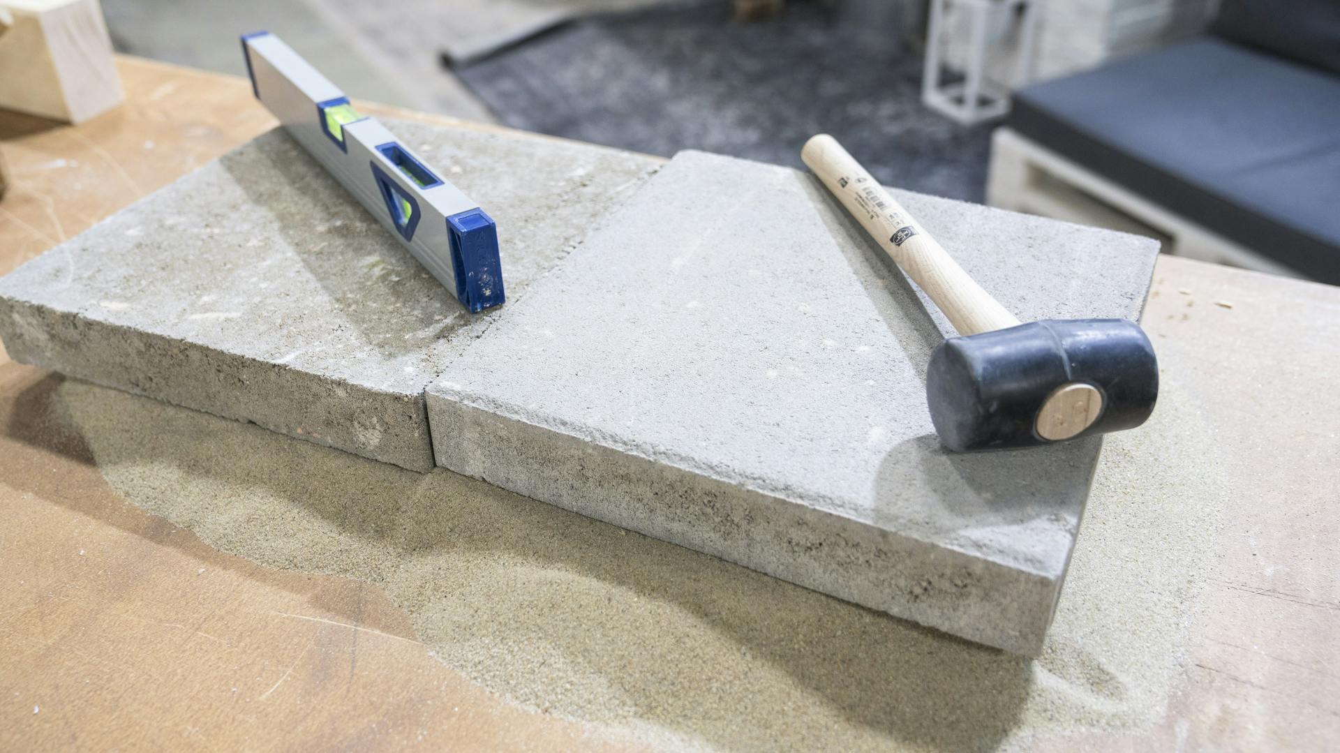 Gummihammer liegt mit Wasserwaage auf Steinplatten.