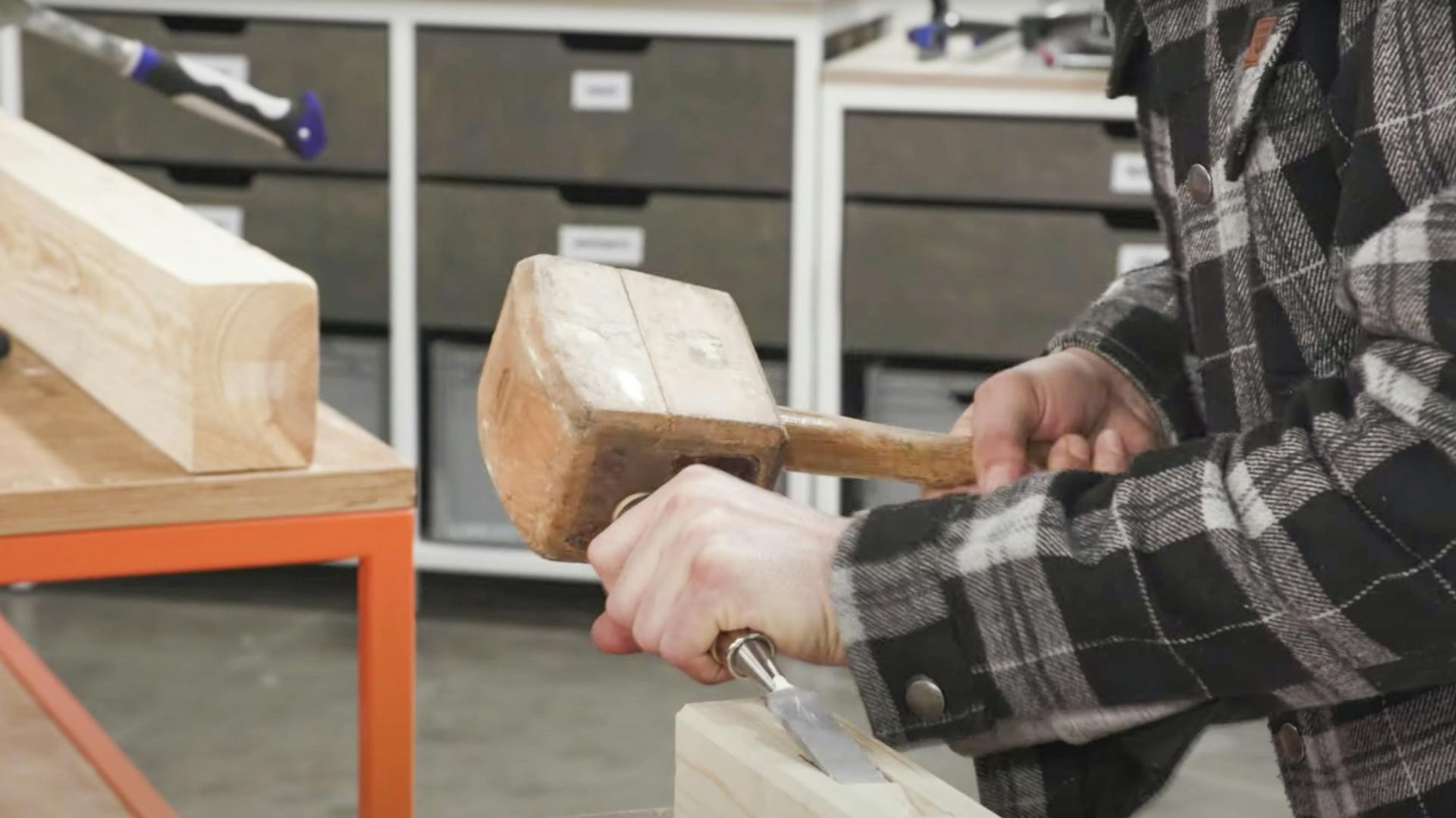 Mann klopft mit Klopfholz und Meißel Holz ab.