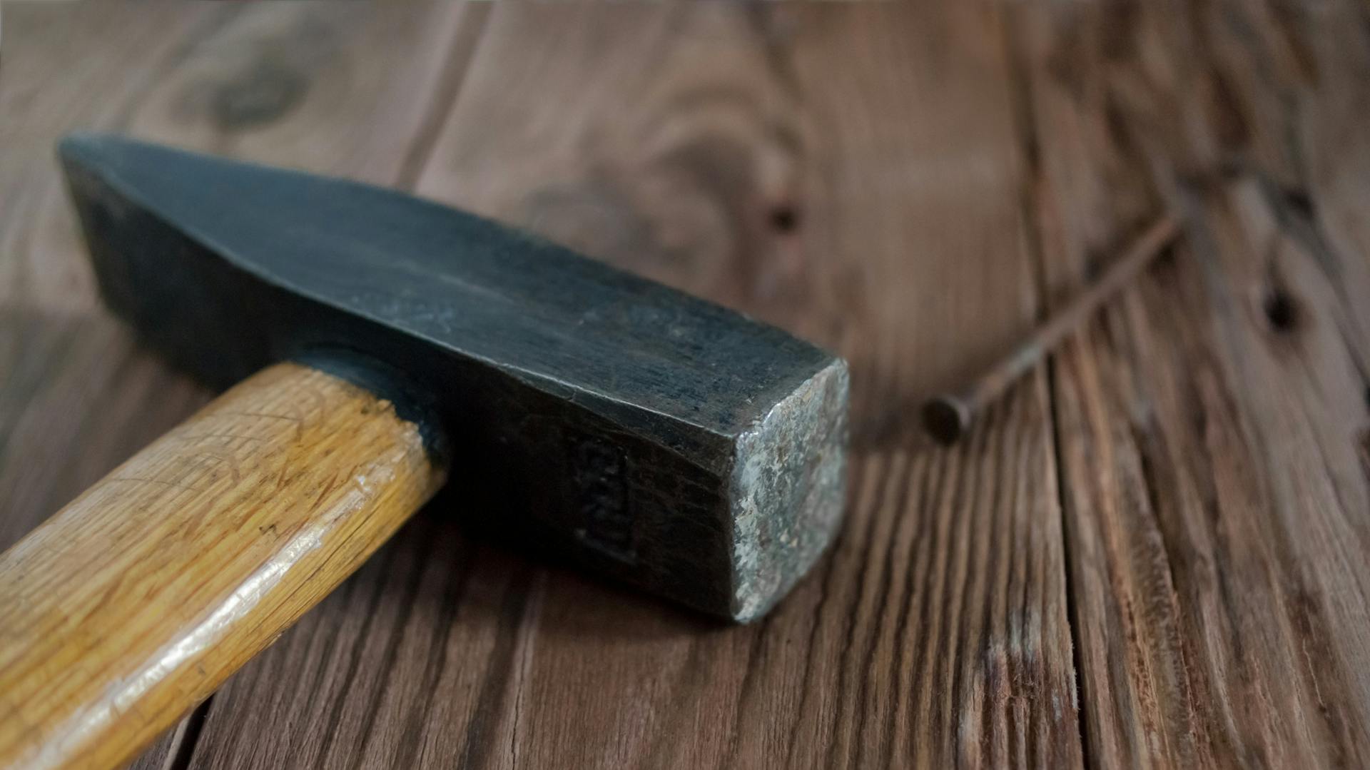 Schlosserhammer liegt mit einem Nagel auf einem Holztisch.