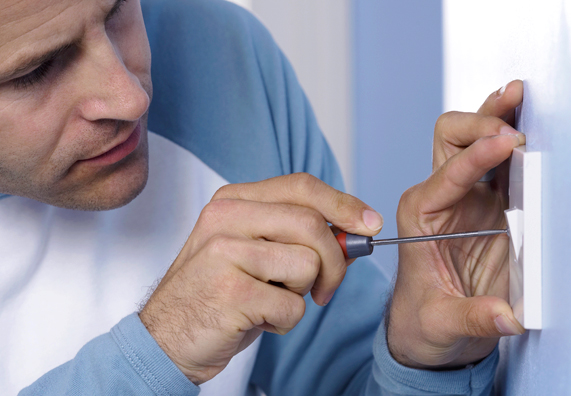 Mann arbeitet mit Schraubendreher an Lichtschalter