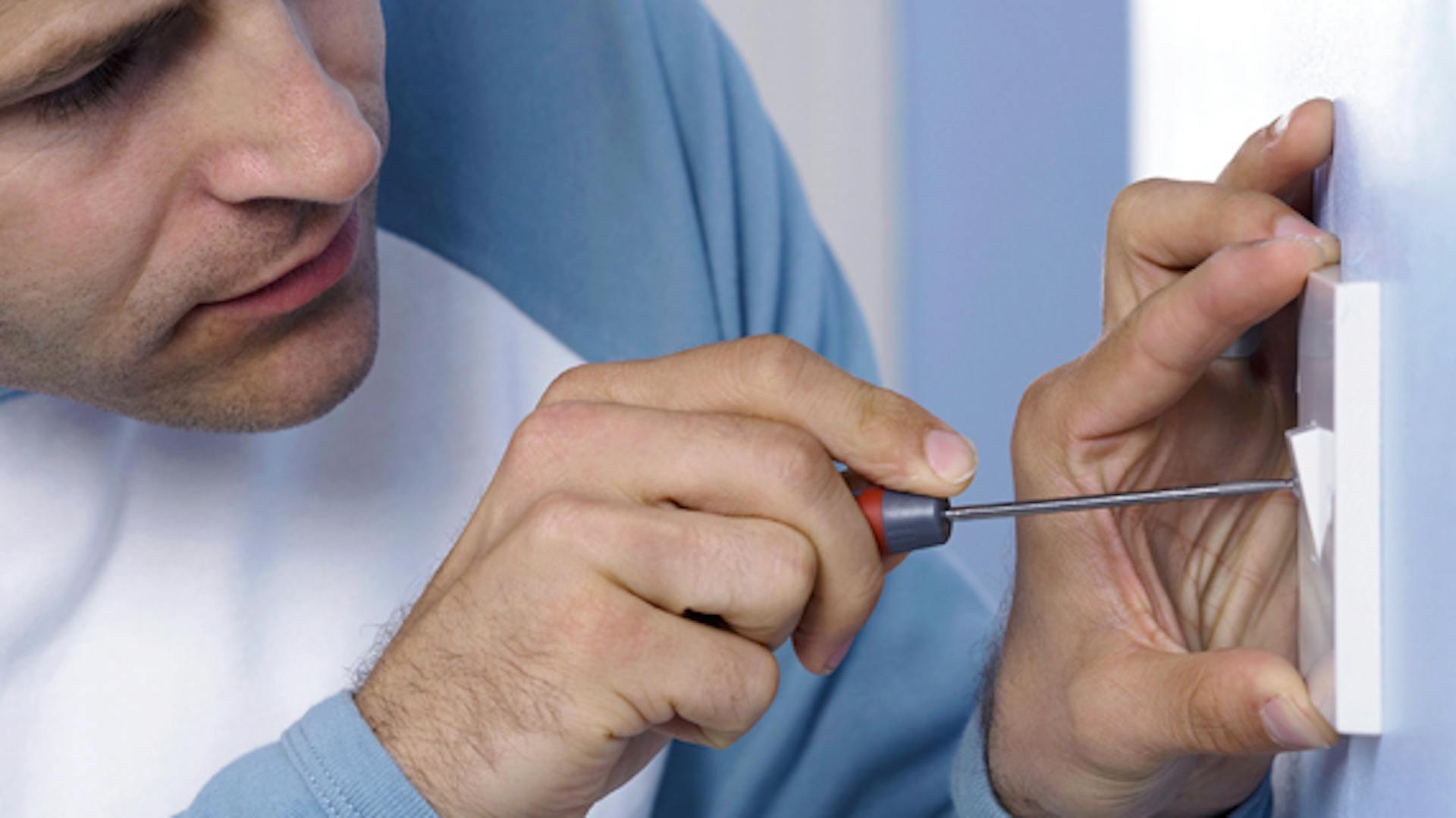 Mann arbeitet mit Schraubendreher an Lichtschalter