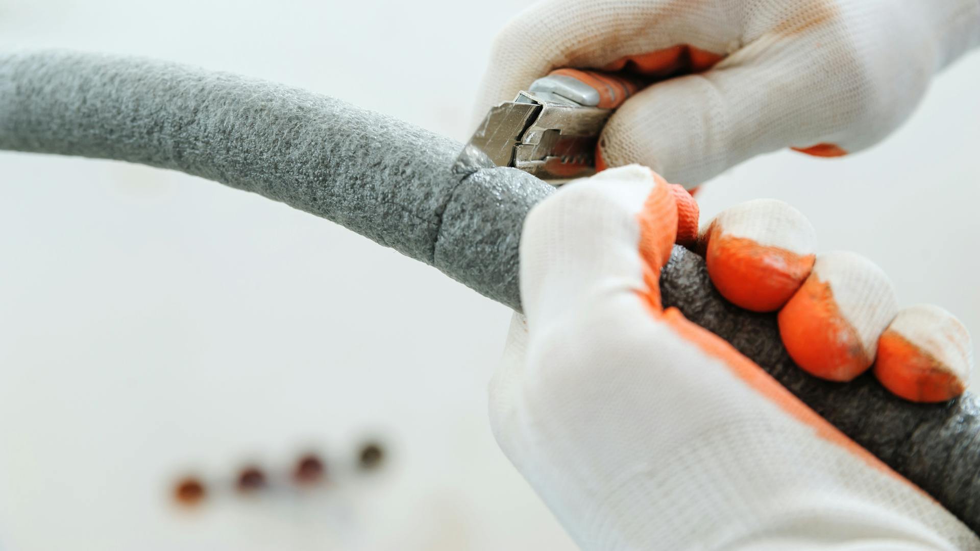 Persona con guanti protettivi e taglierino recide un isolante in feltro.