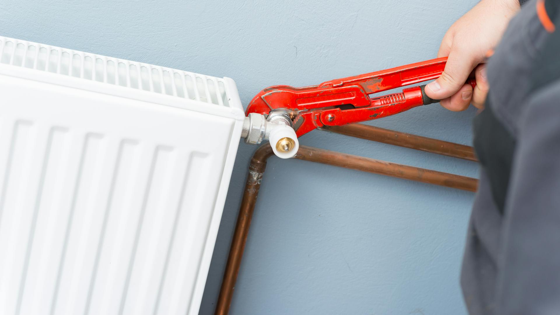Ein Heizungsventil wird mit einer roten Rohrzange gegriffen.