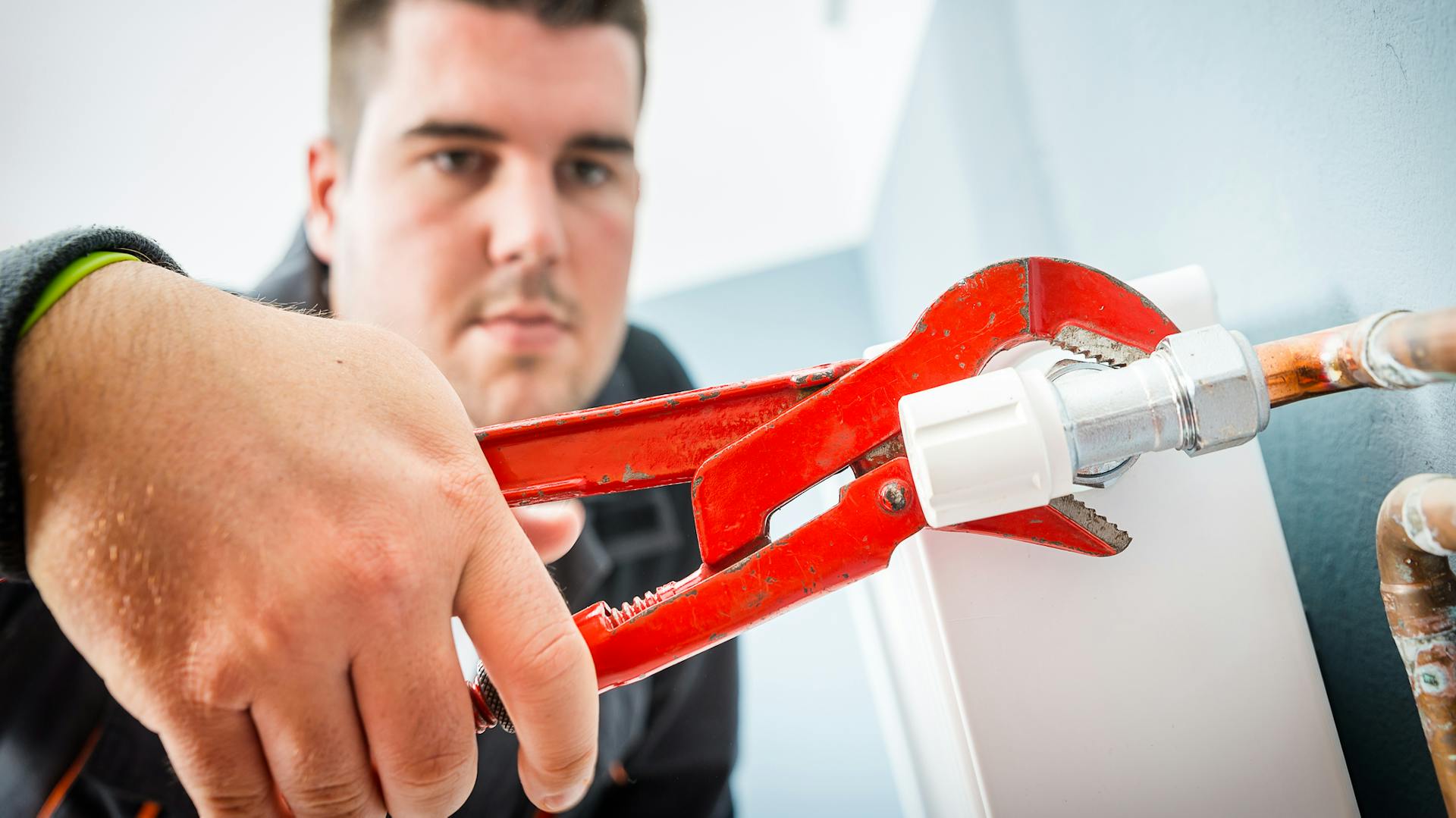 Ein Mann schraubt ein Heizungsventil mit einer Rohrzange fest.