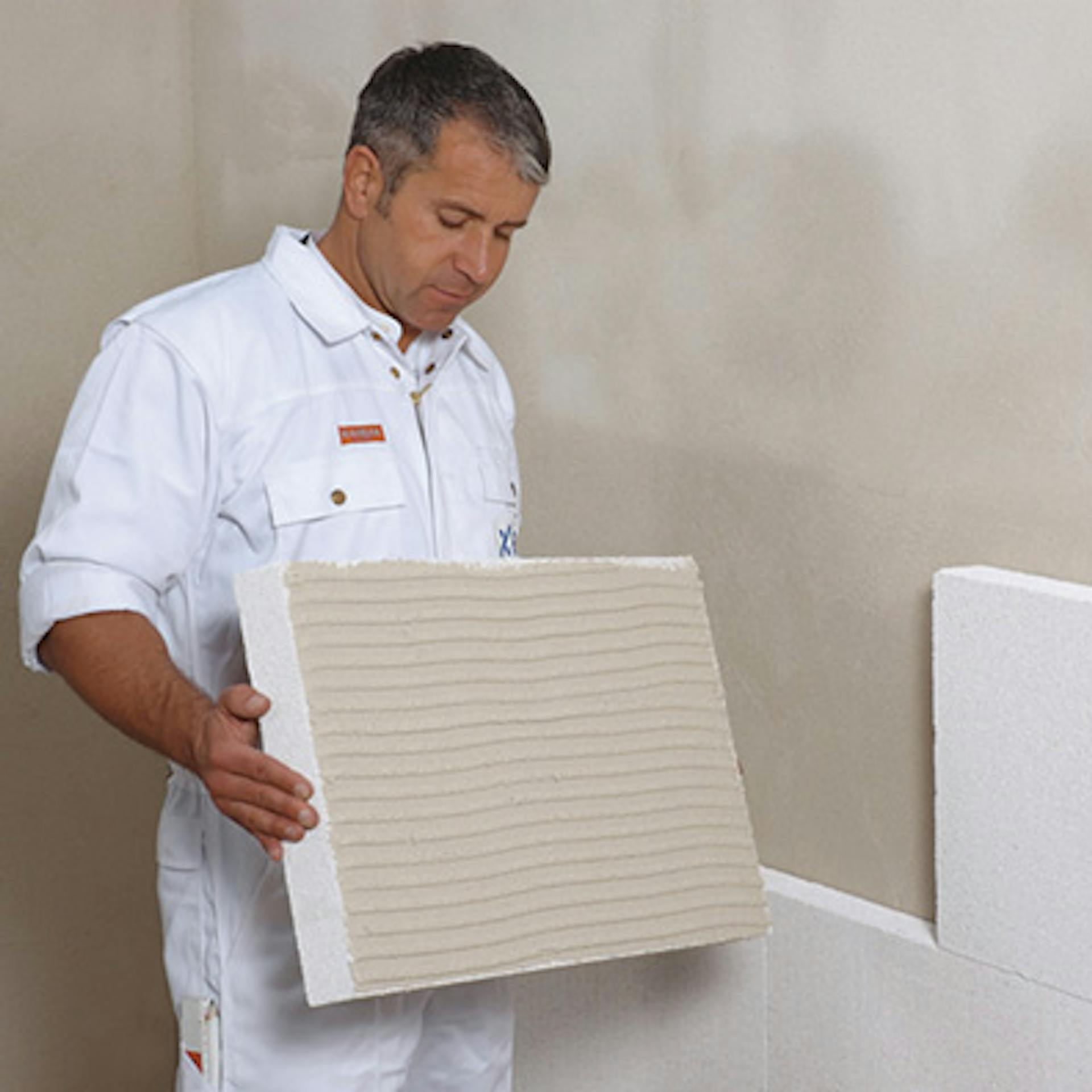 Egy barkácsoló szigetelőlapokat helyez fel egy belső falra.