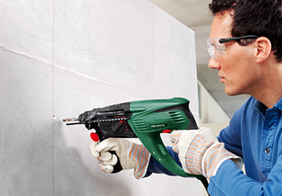 Egy barkácsoló fúrógéppel készít furatot teher rögzítéséhez a belső fal szigetelésén.